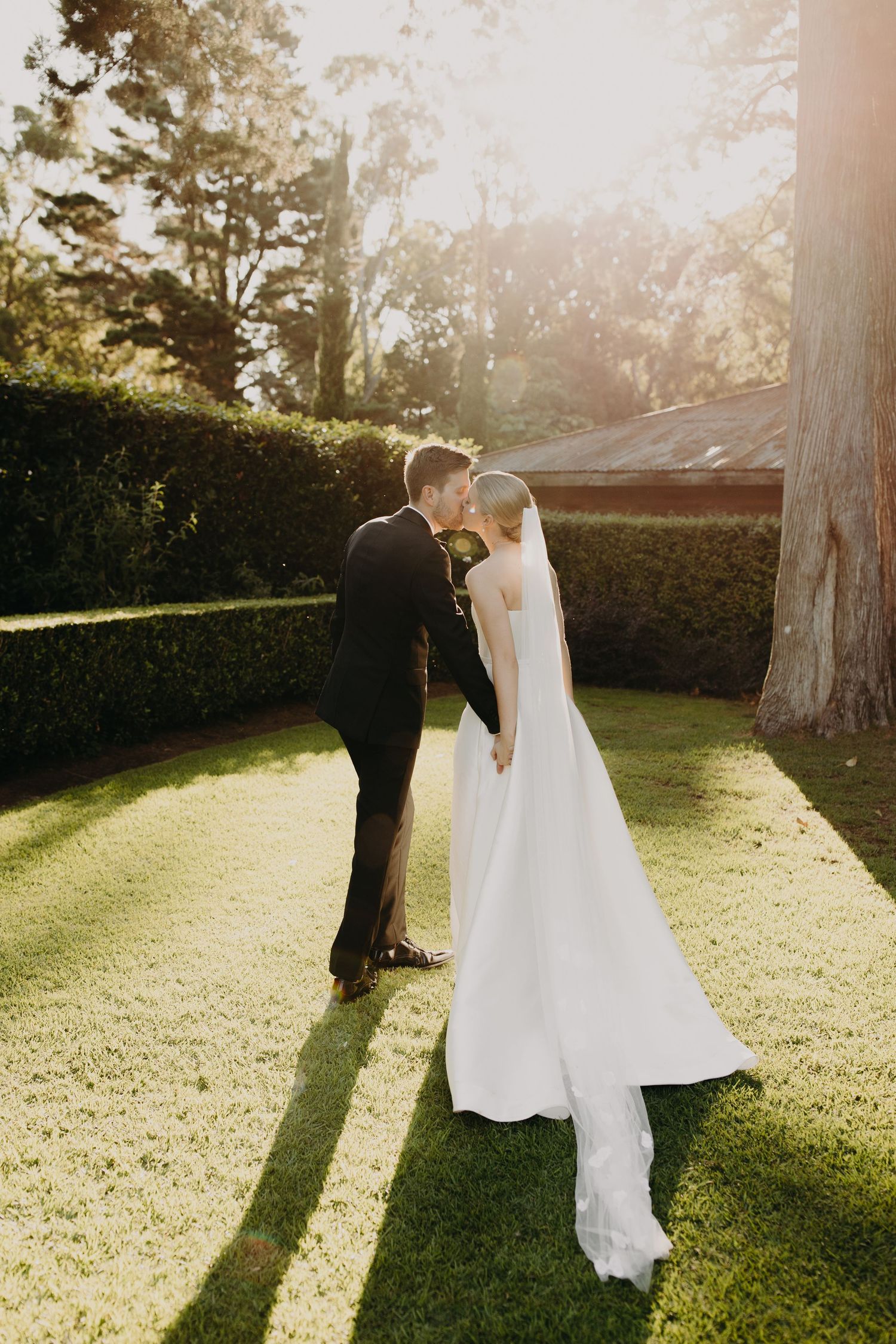 A romantic sunset wedding portrait on a manicured lawn with long shadows.