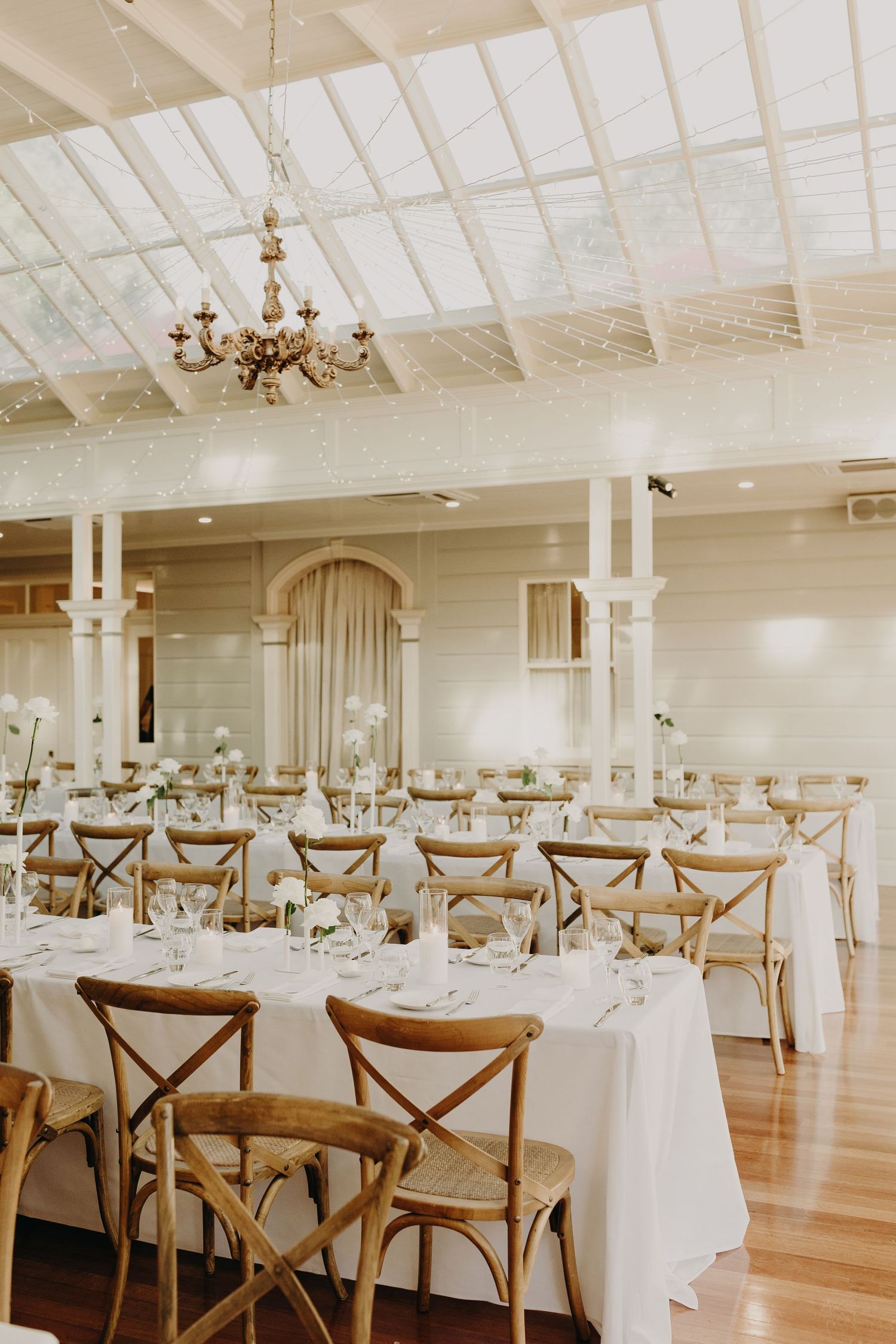 An elegant white reception hall with cross-back chairs and round tables set for a wedding.