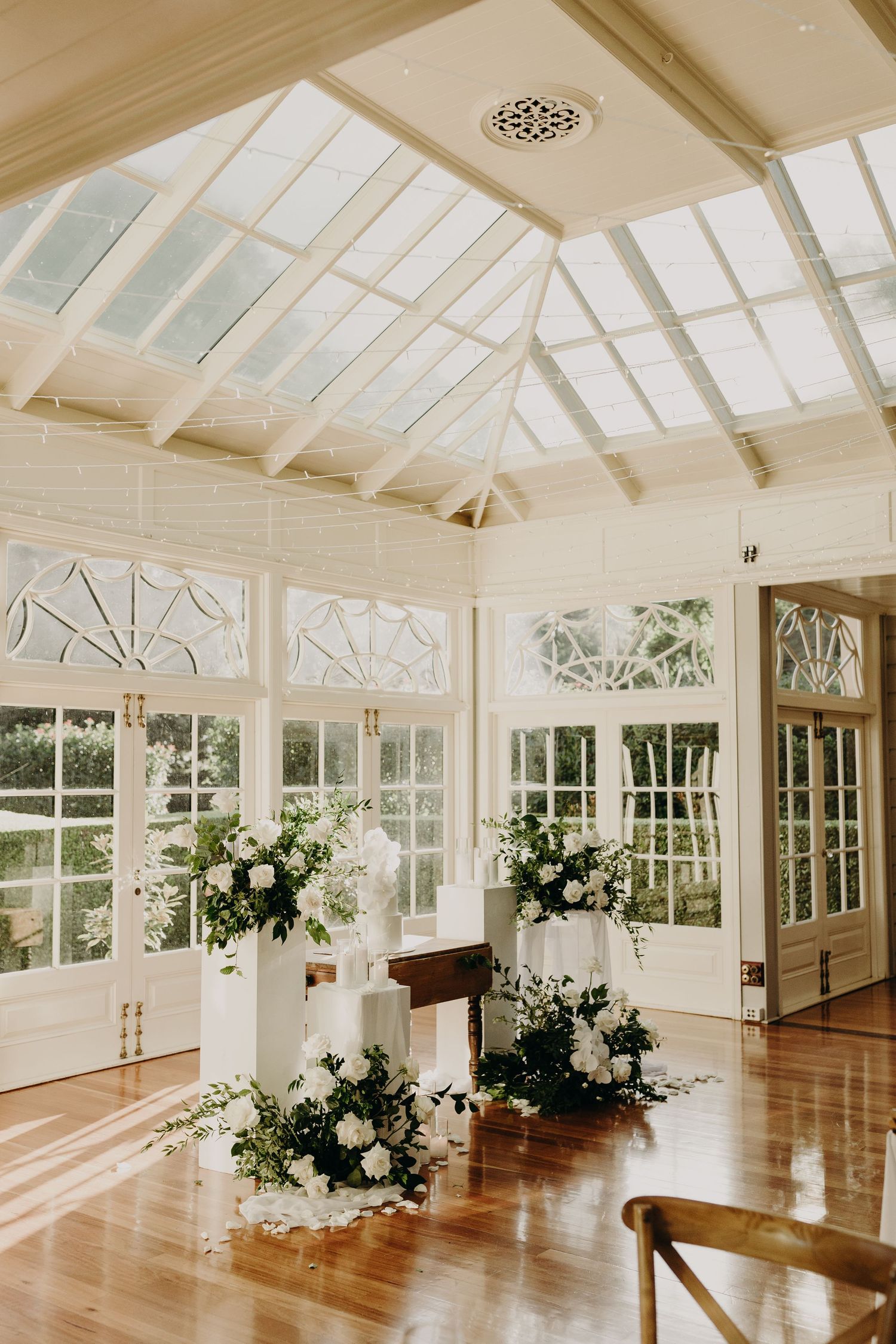 A bright conservatory wedding venue with white walls, skylights and elegant floral decorations.