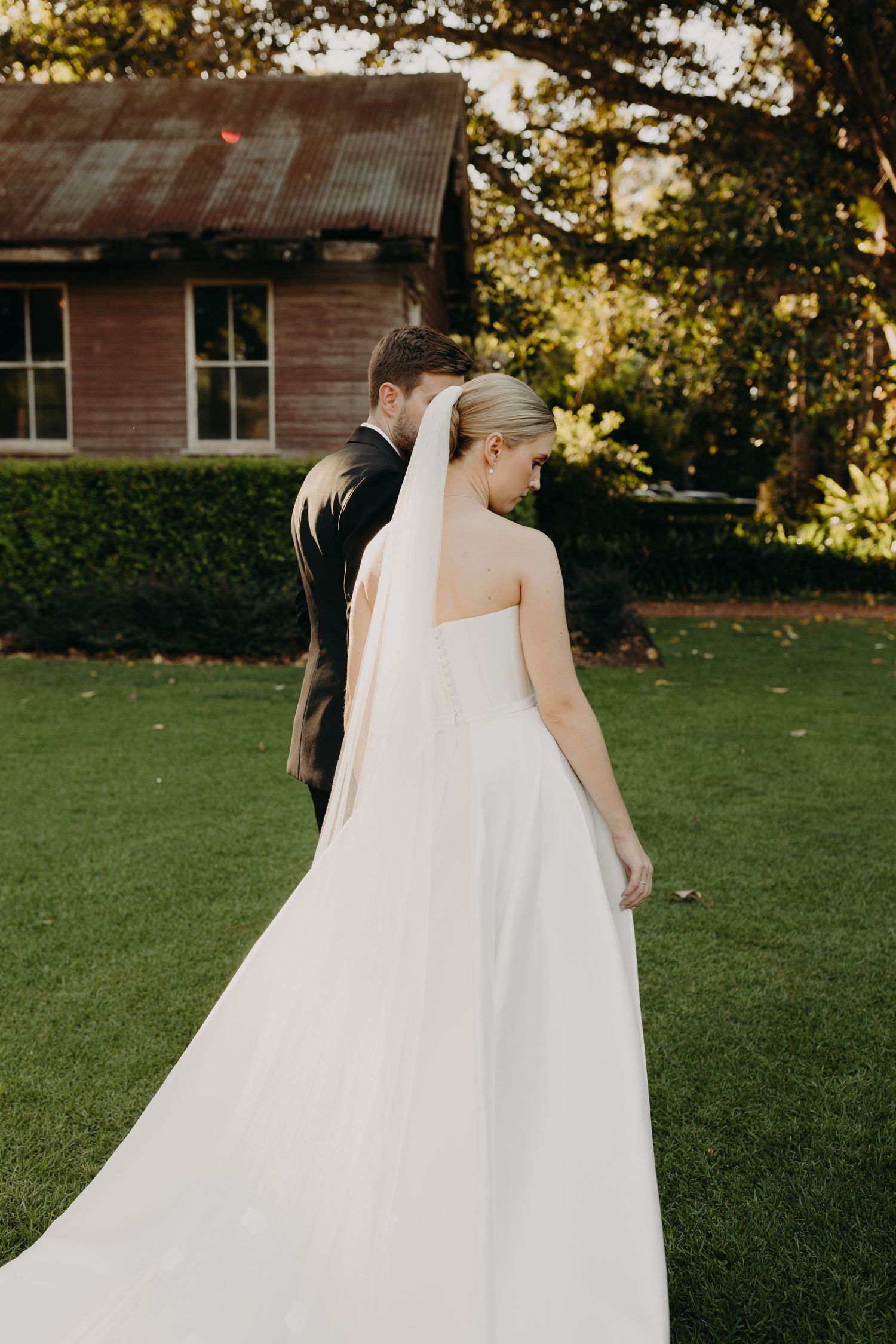 A wedding couple walks together on a green lawn during golden hour photography.
