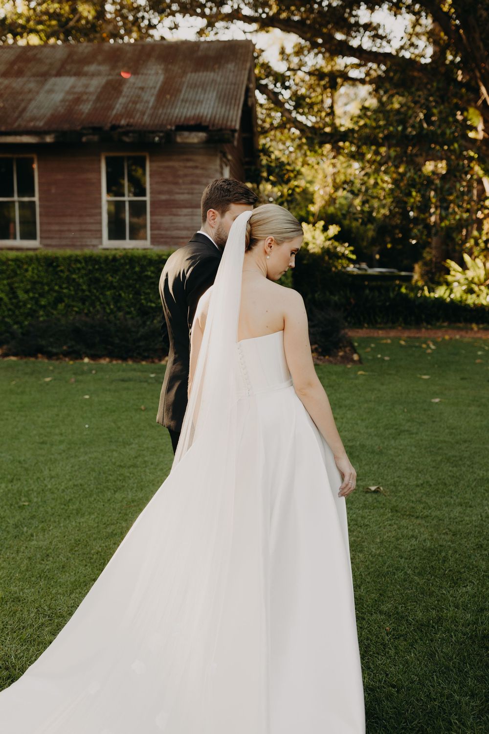 A wedding couple walks together on a green lawn during golden hour photography.