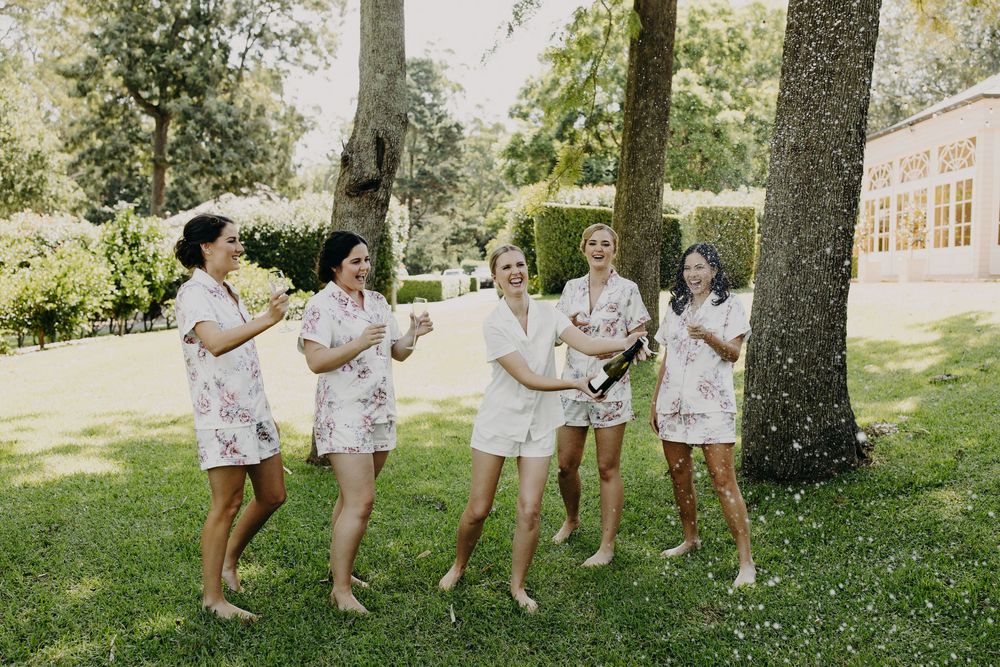 Group wearing matching floral robes dancing playfully outdoors under trees.
