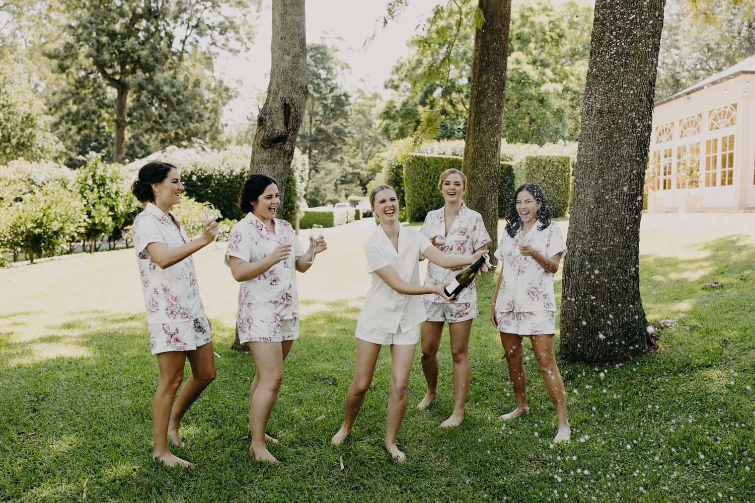 Group wearing matching floral robes dancing playfully outdoors under trees.