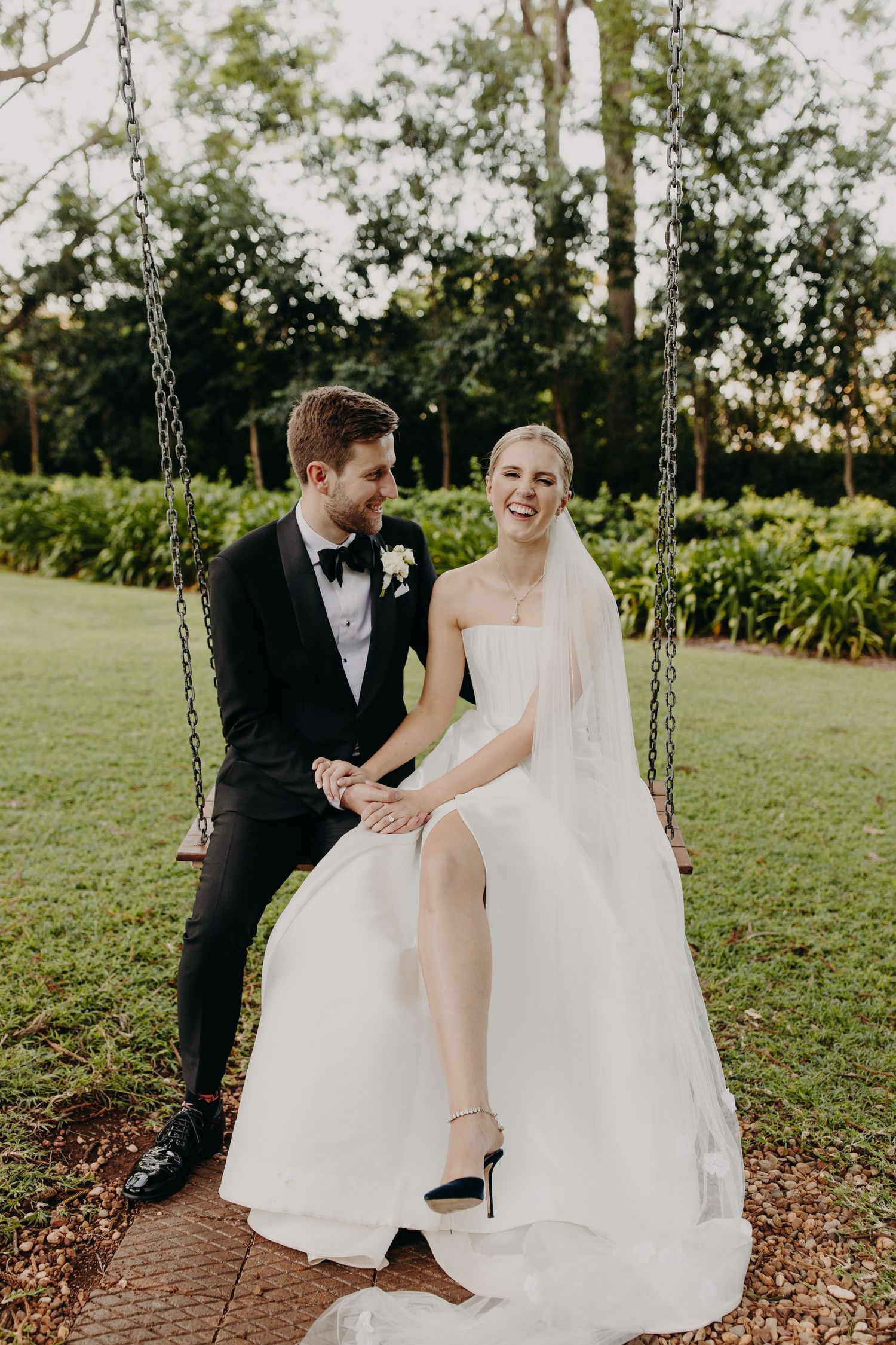 Joyful wedding couple shares playful moments on garden swings during photo session.