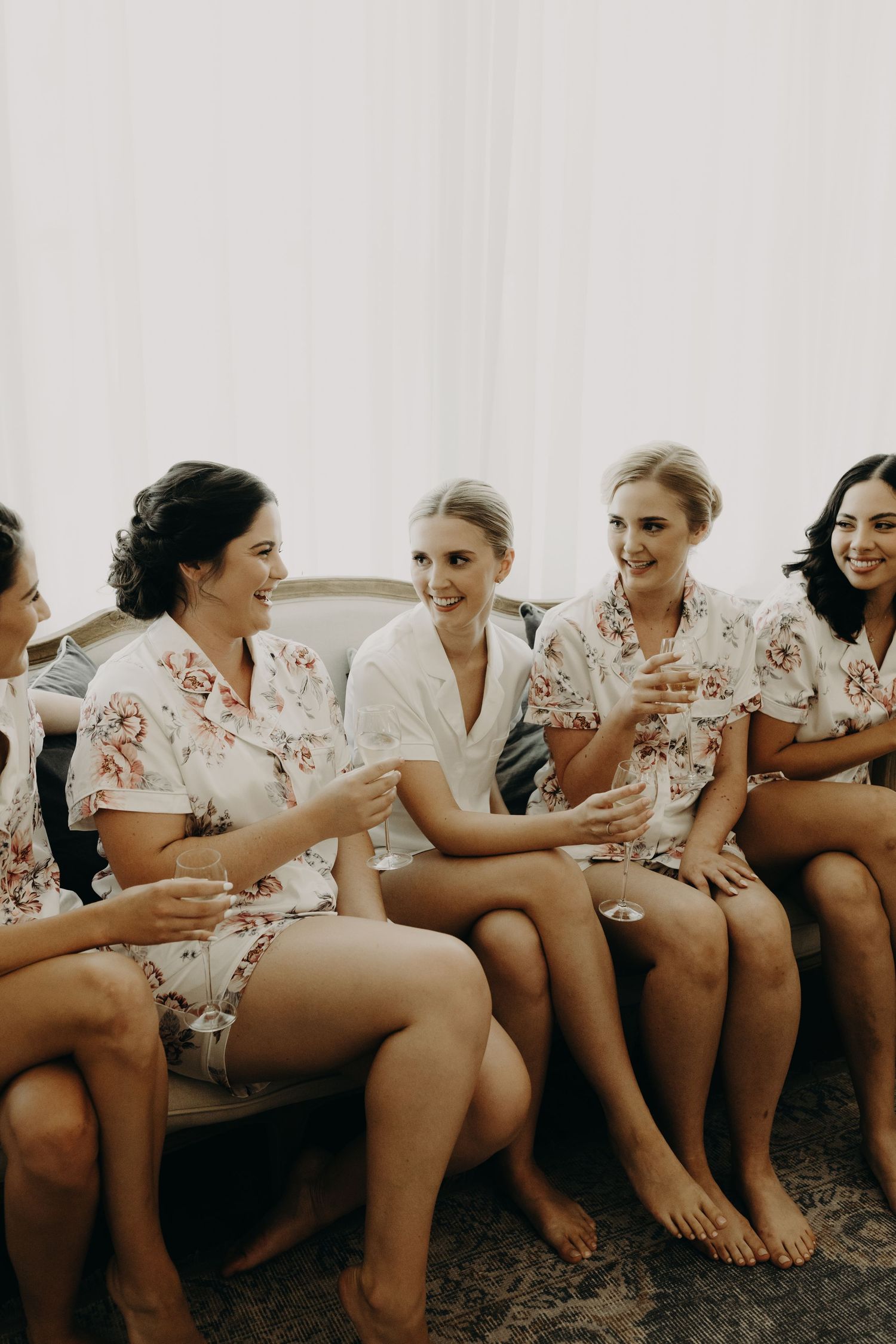 Candid moment of wedding party in floral robes sharing laughter on a couch.