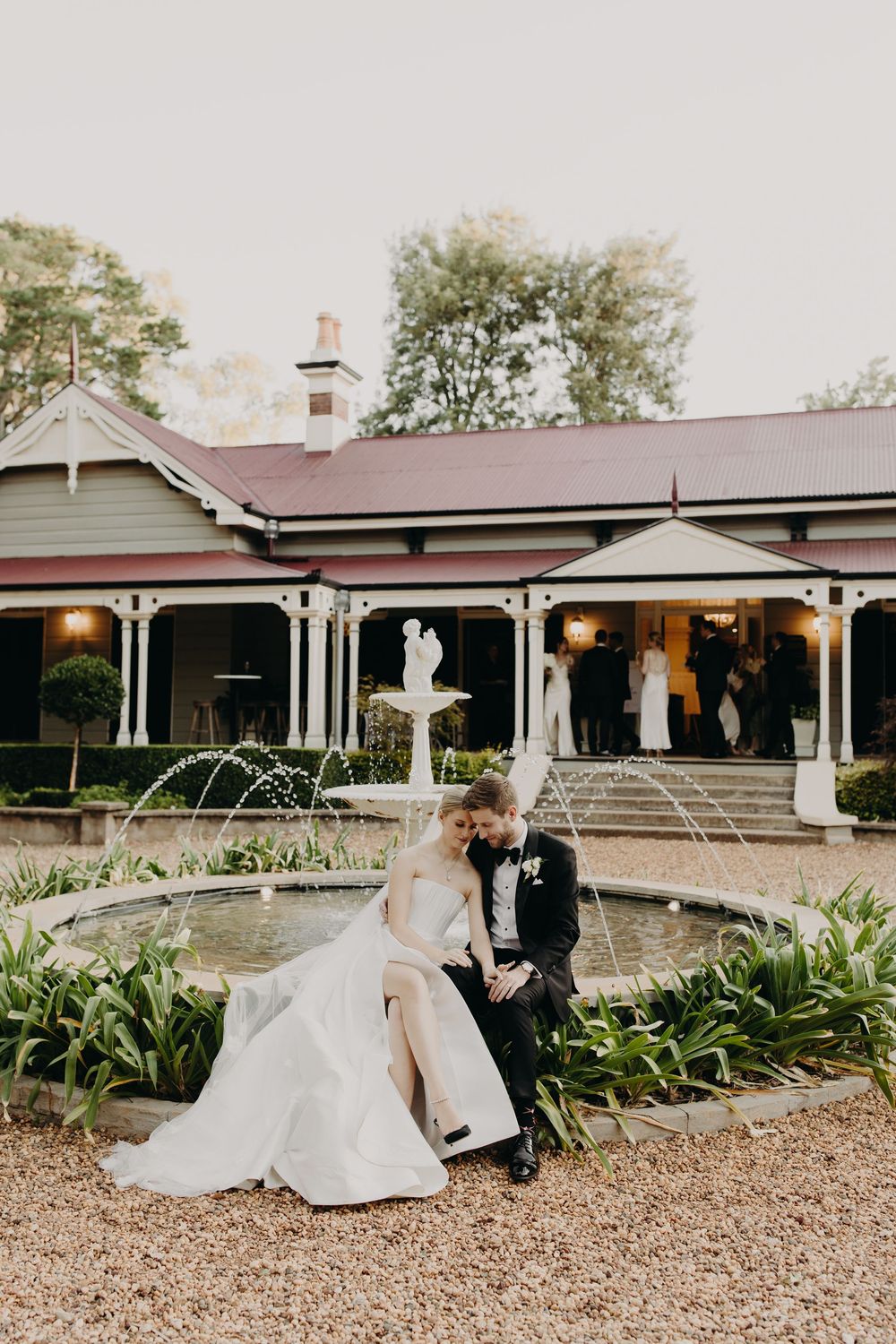Elegant wedding venue exterior with fountain and gravel path leading to covered porch.