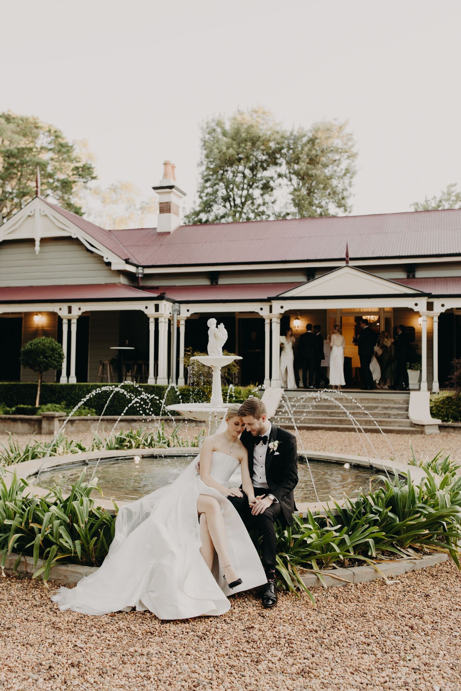 Elegant wedding venue exterior with fountain and gravel path leading to covered porch.