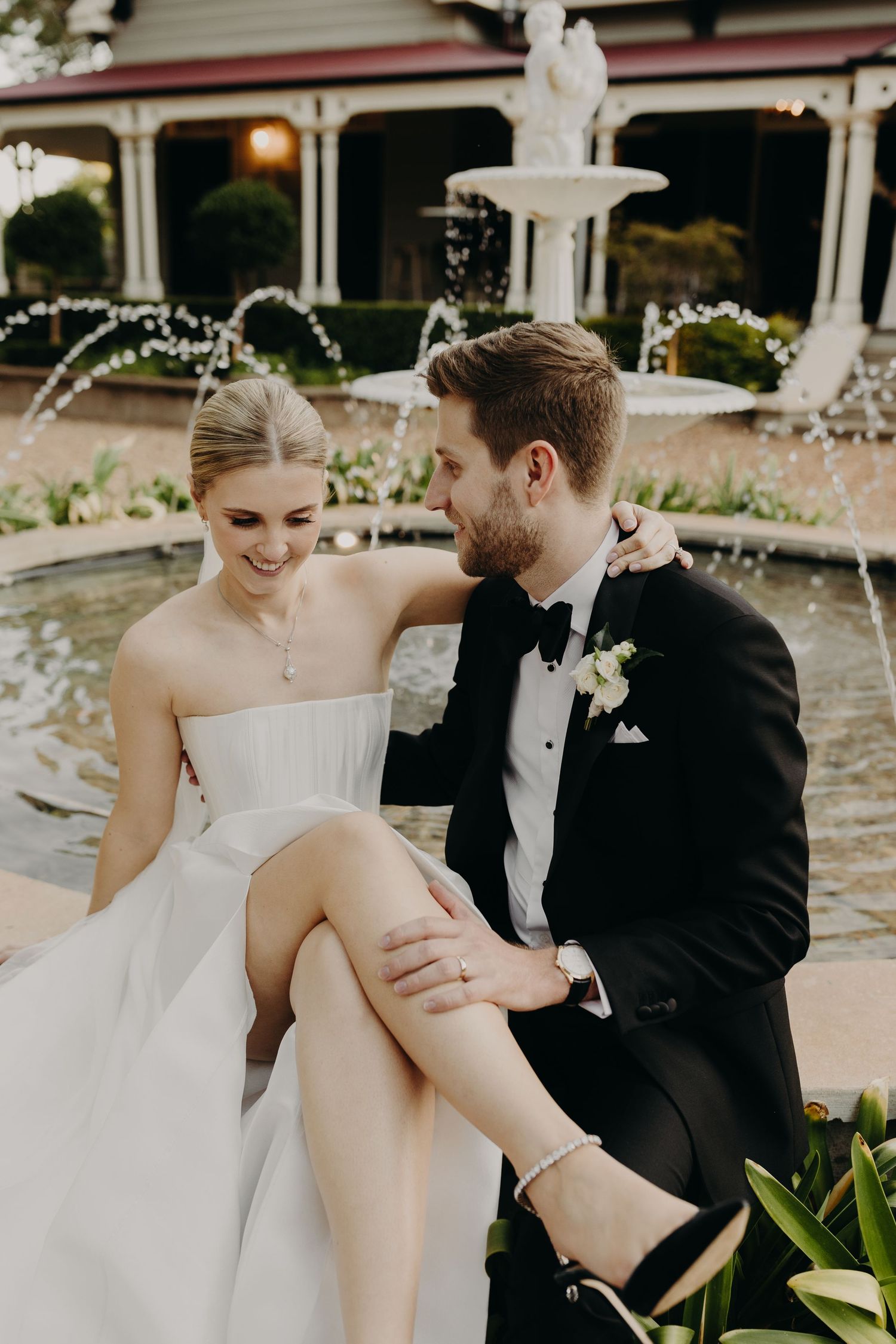 Romantic wedding couple moment captured by fountain outside historic venue.