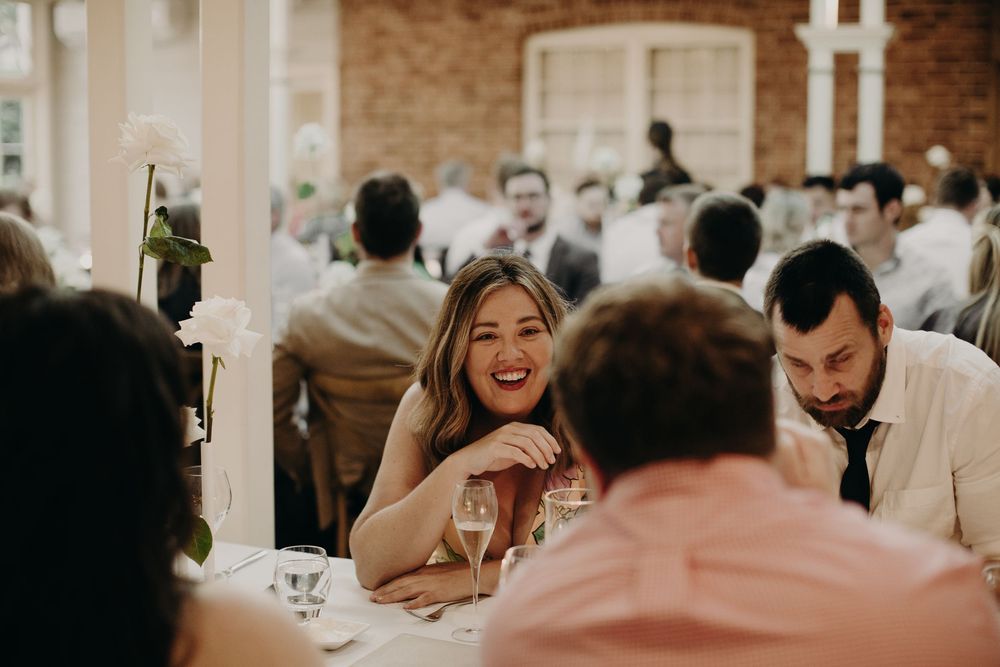 Wedding reception dinner in warm-lit venue with guests seated at decorated tables.