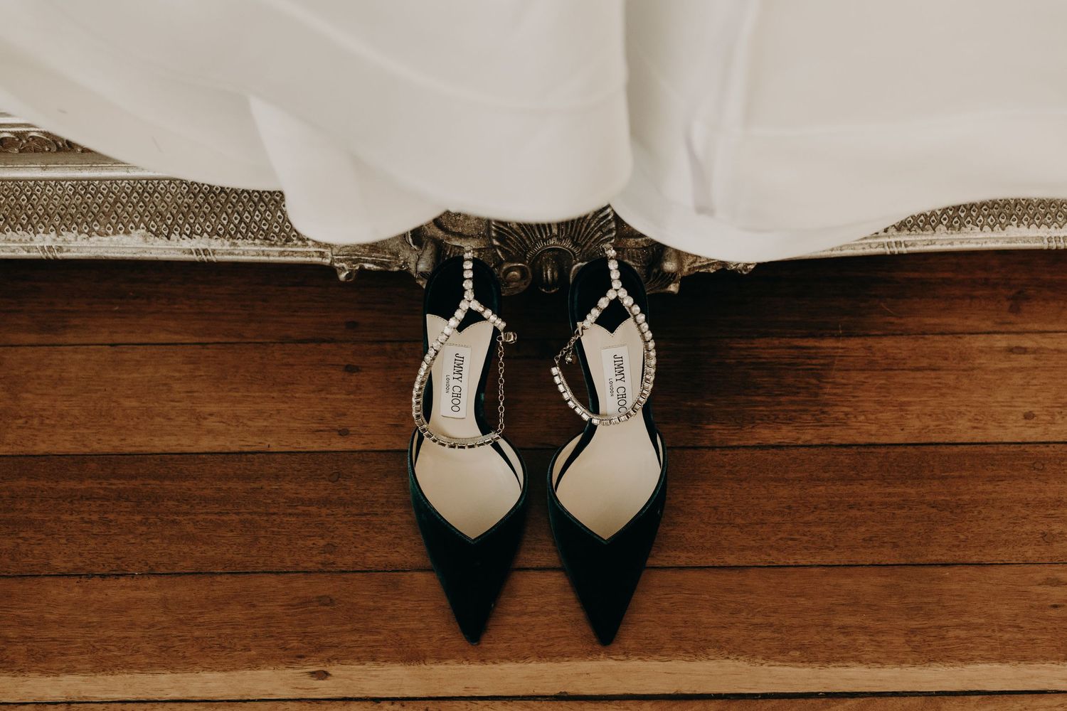 Wedding shoes and dress hem details on wooden flooring.