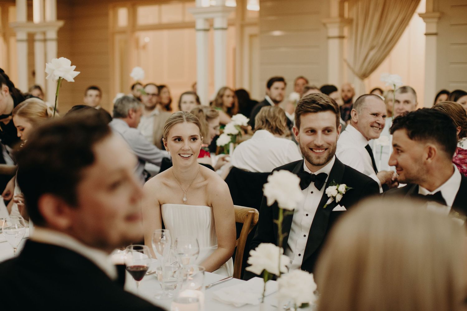 Candid reception scene with guests dining at elegant tables in warm ambient lighting.