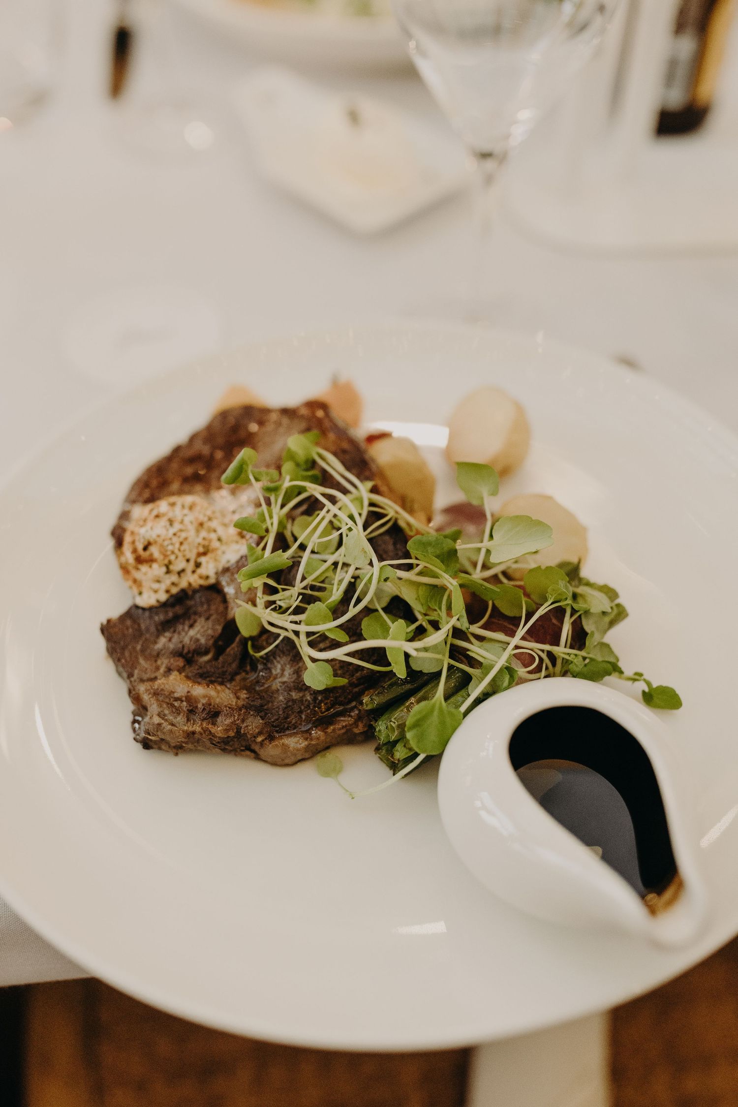 Gourmet steak dish garnished with microgreens and sauce served on a white plate.