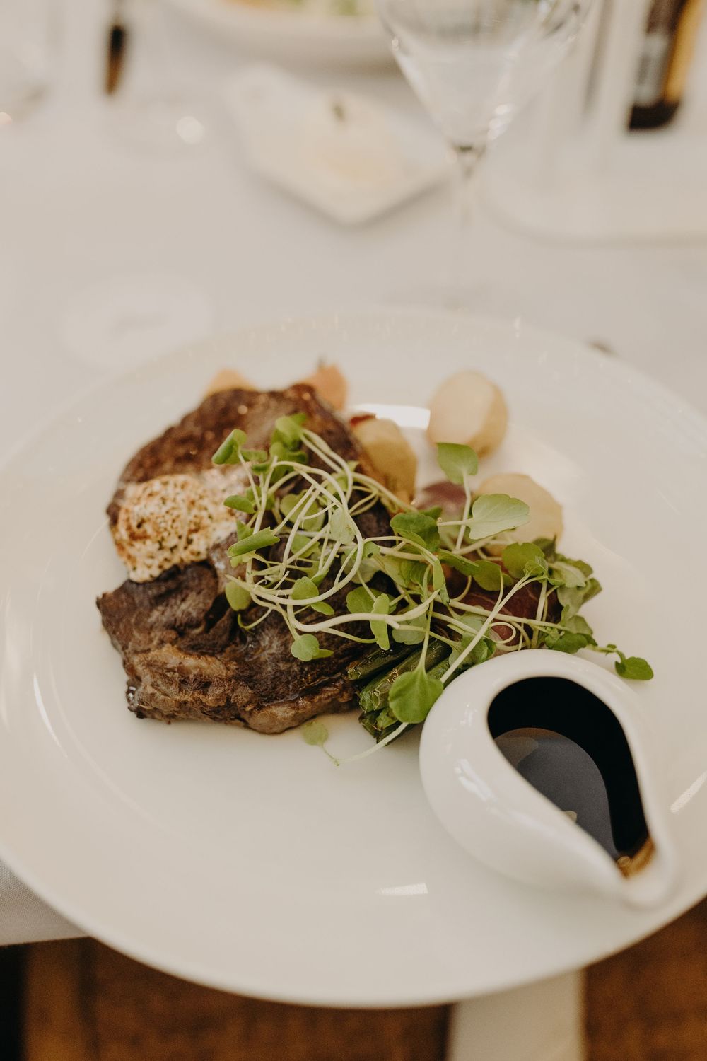 Gourmet steak dish garnished with microgreens and sauce served on a white plate.