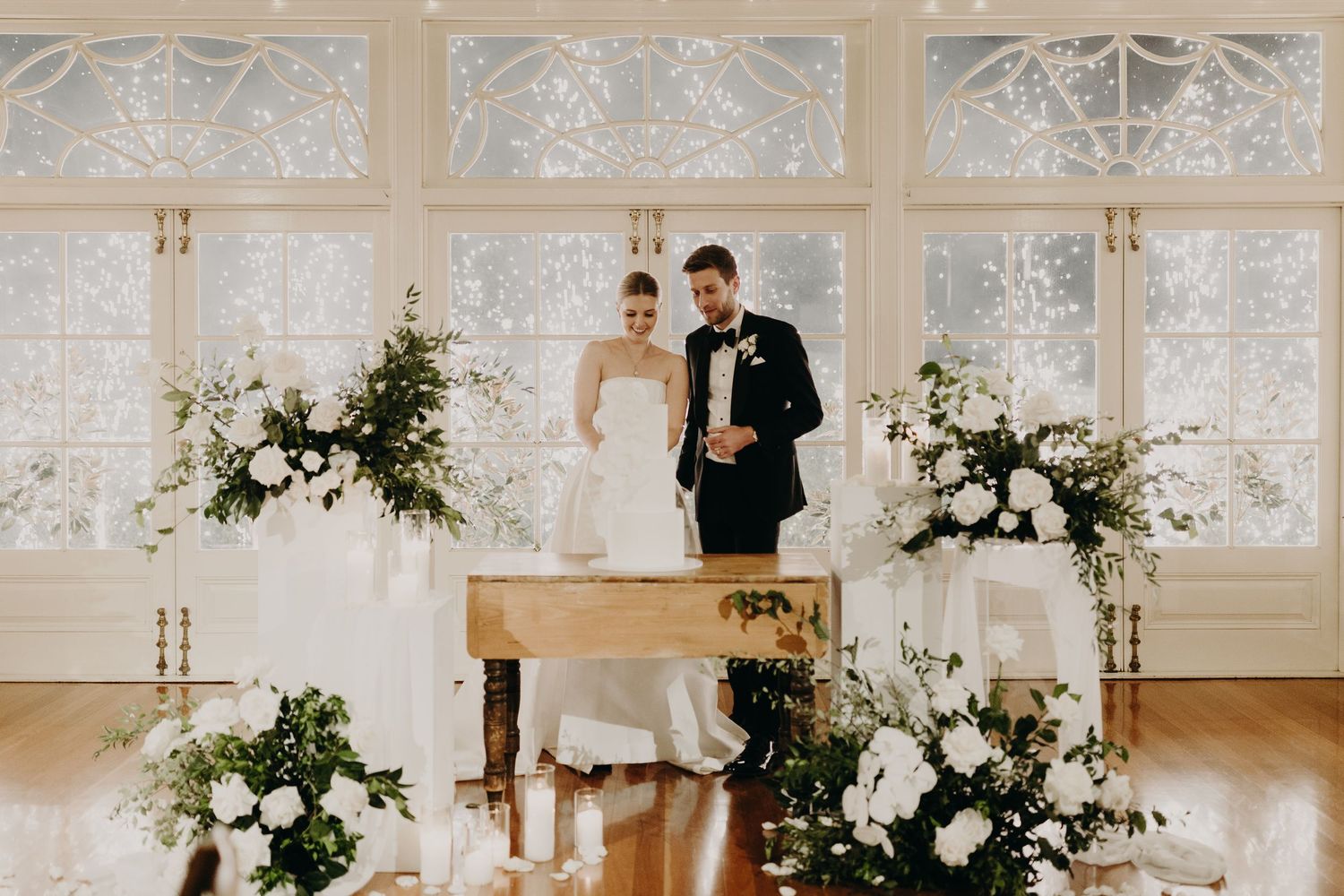Wedding ceremony setup with piano and floral arrangements in front of ornate windows.