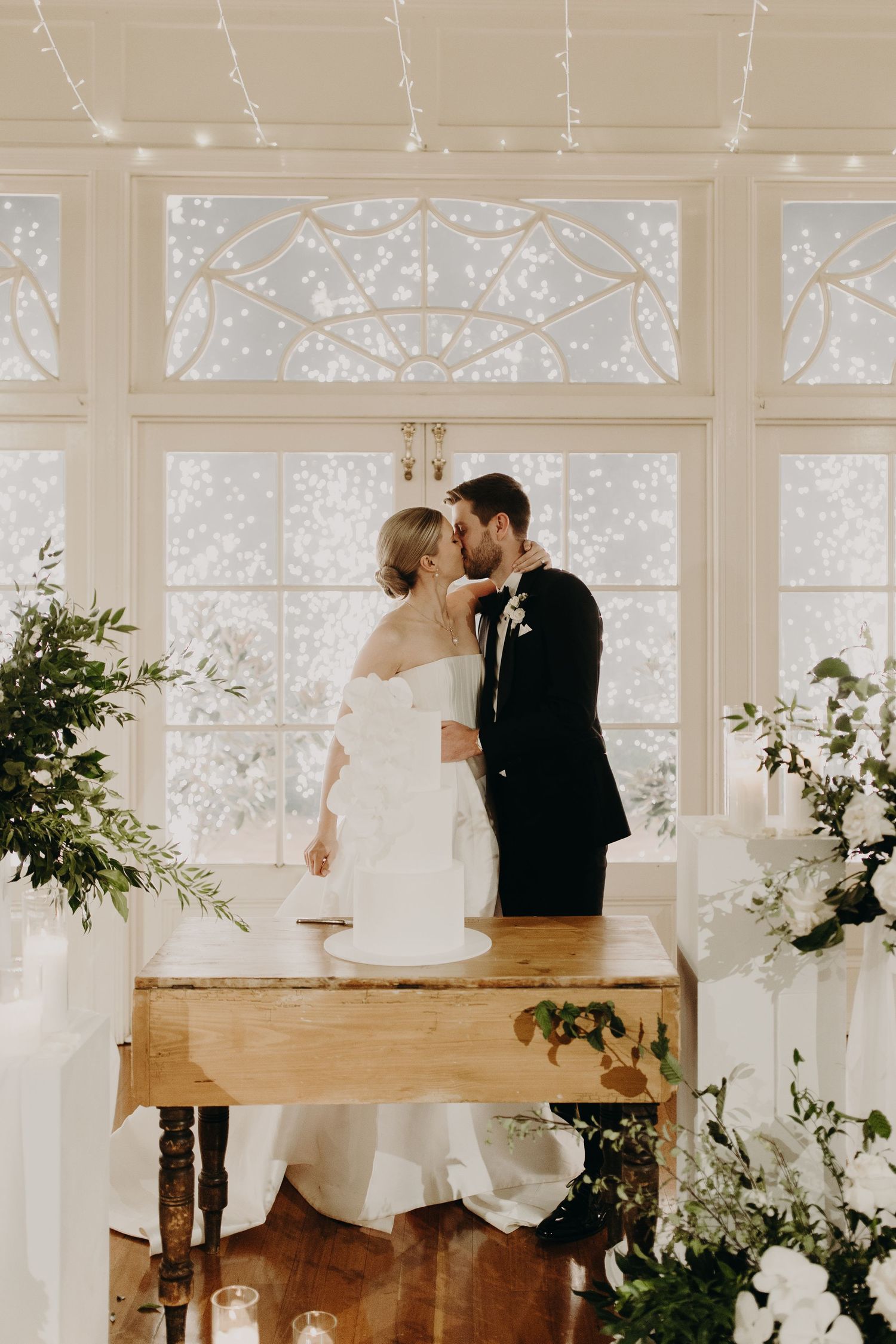 Romantic moment captured in front of decorative windows with white floral arrangements.