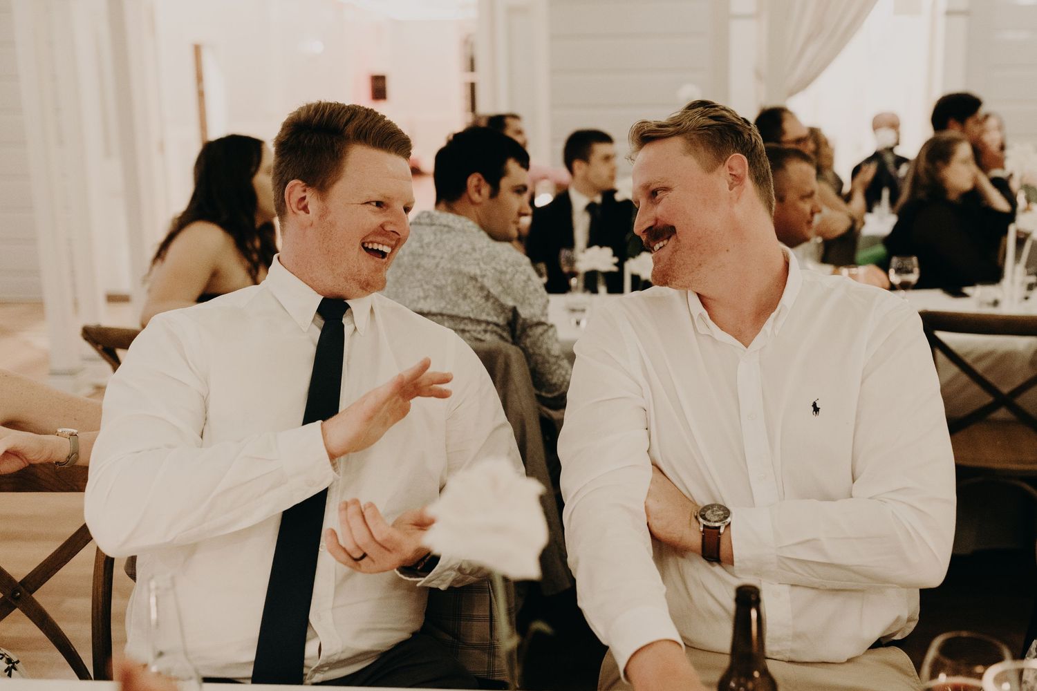 Two guests in white shirts share a laugh during the wedding reception.