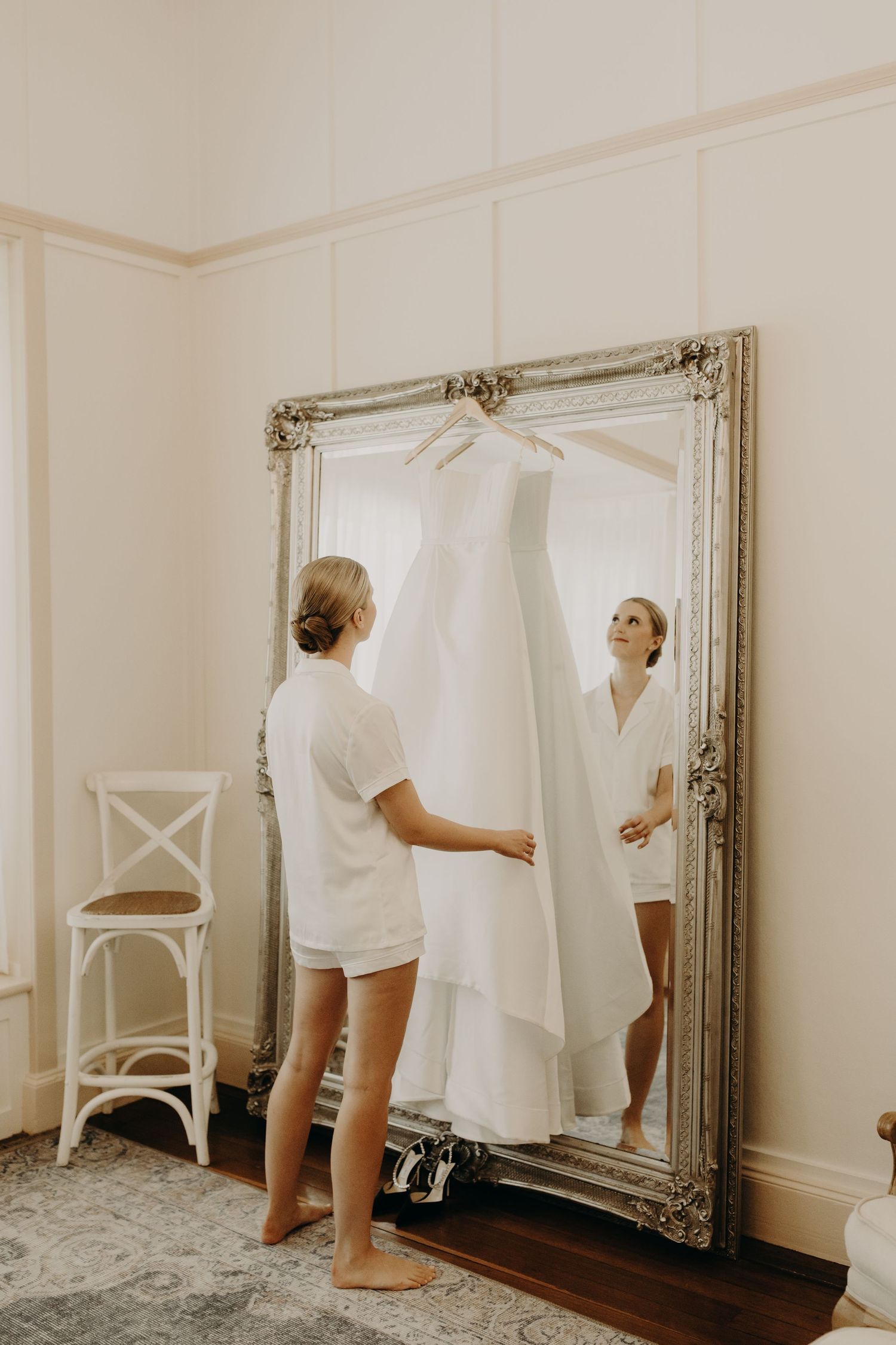 Wedding dress preparation scene with ornate mirror and white decor.