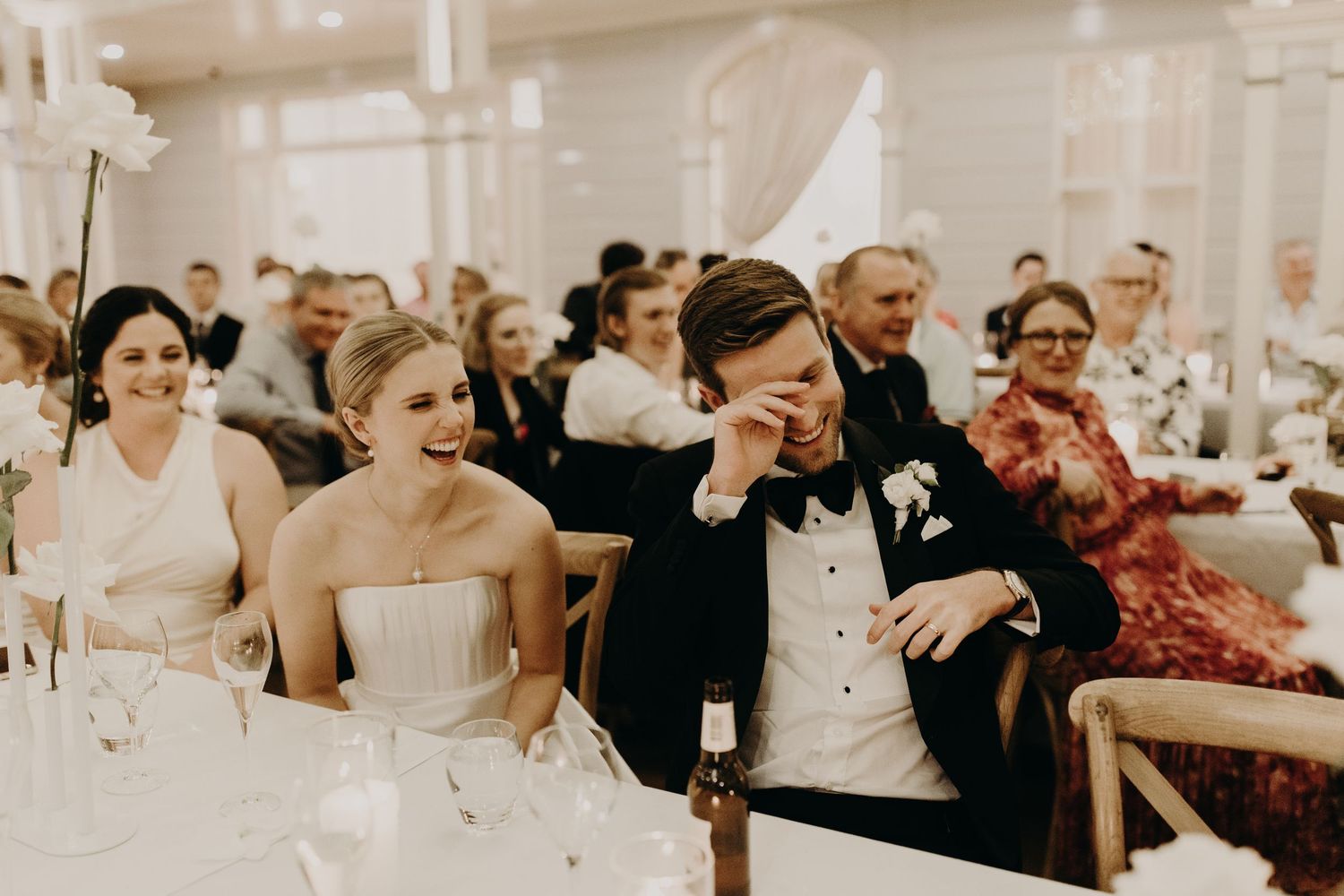 Wedding reception guests react emotionally during speeches at an indoor venue.