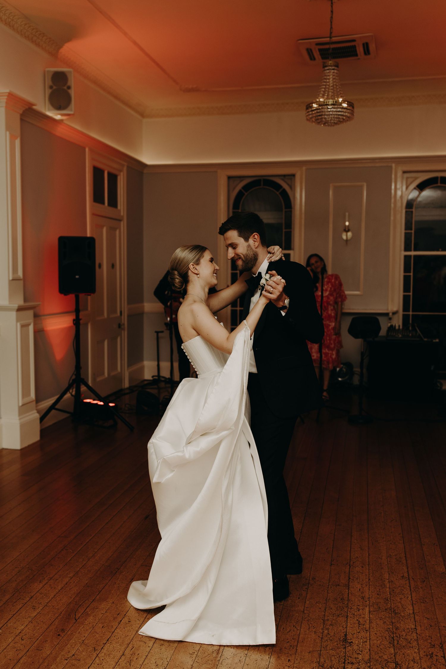 A couple performs an elegant dance move in a spacious ballroom with wooden floors.