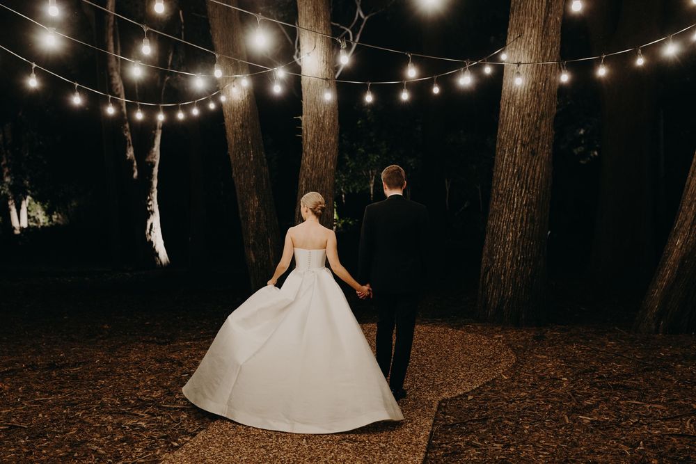 Outdoor wedding scene with string lights illuminating a wooded area at night.