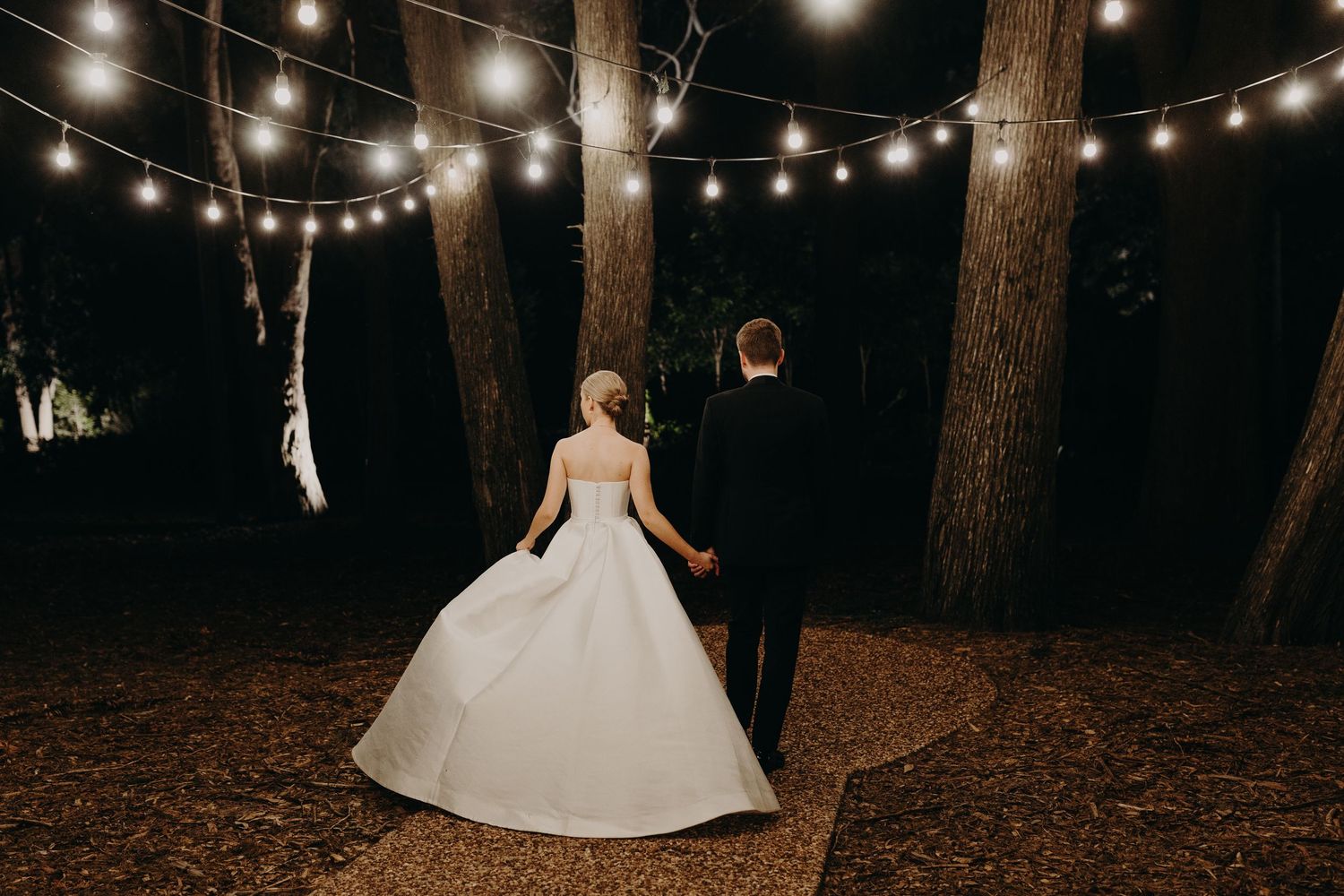 Outdoor wedding scene with string lights illuminating a wooded area at night.