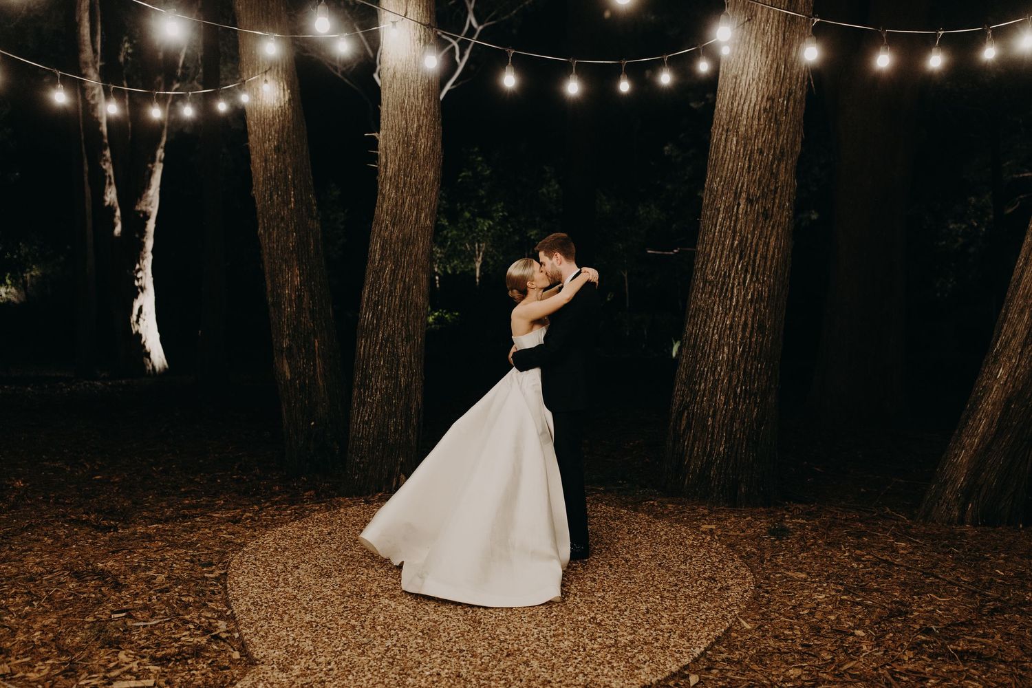 String lights create a romantic ambiance between tall trees during an evening celebration.