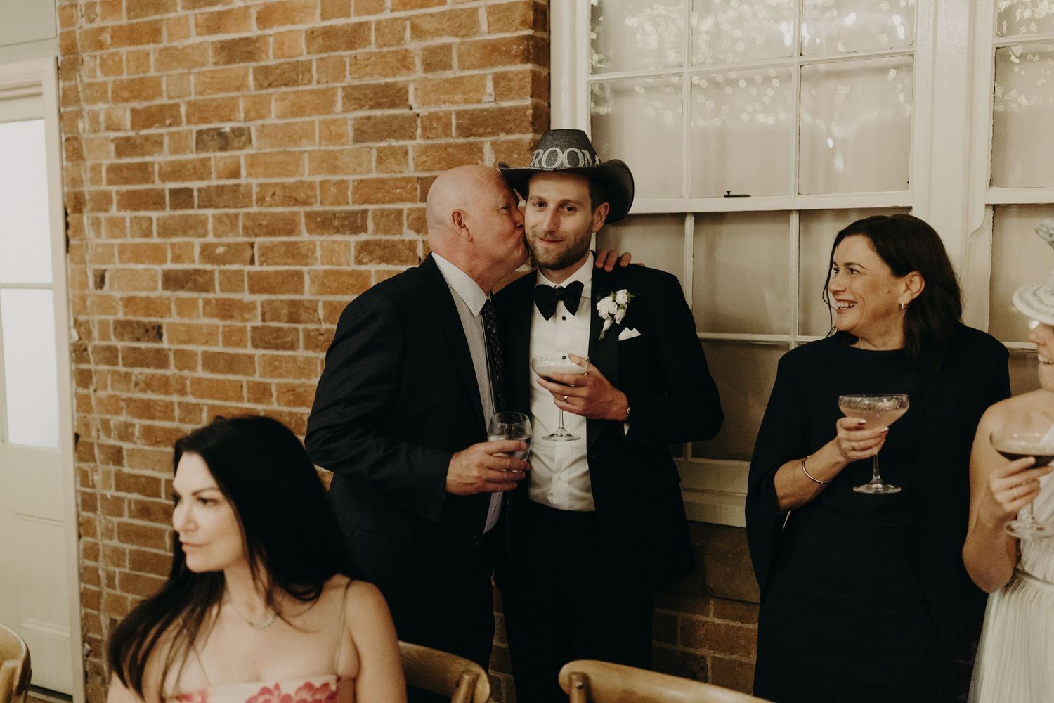 Wedding reception guests mingling in front of exposed brick walls with white trim windows.