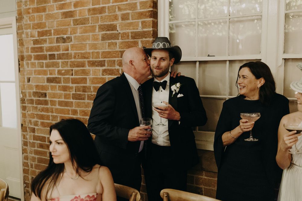 Wedding reception guests mingling in front of exposed brick walls with white trim windows.