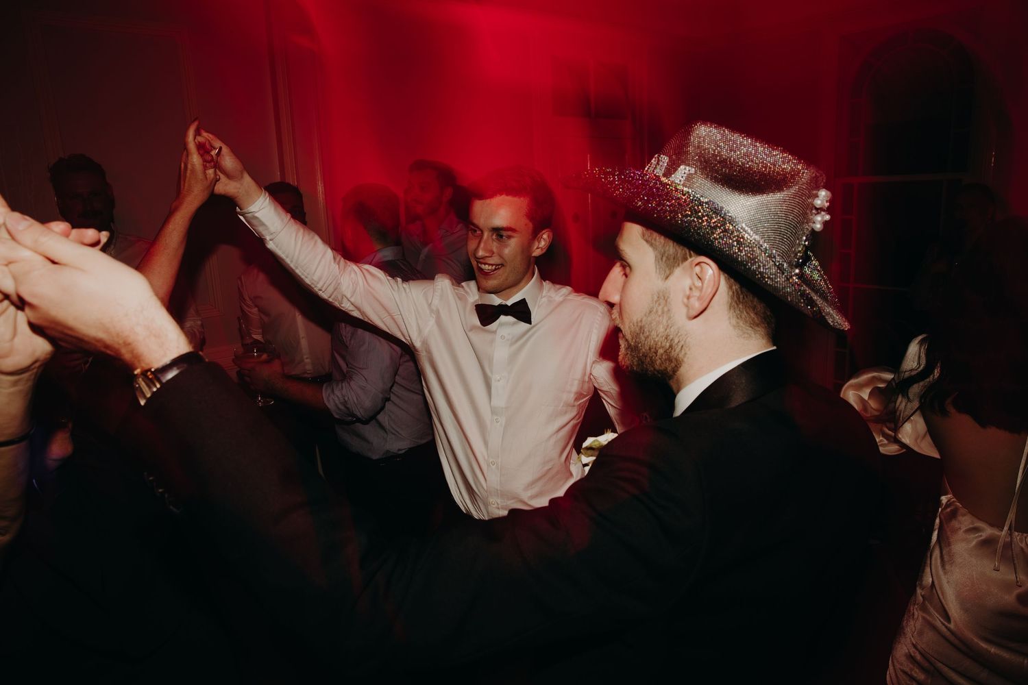 Wedding party dancing and celebrating under dramatic red lighting.