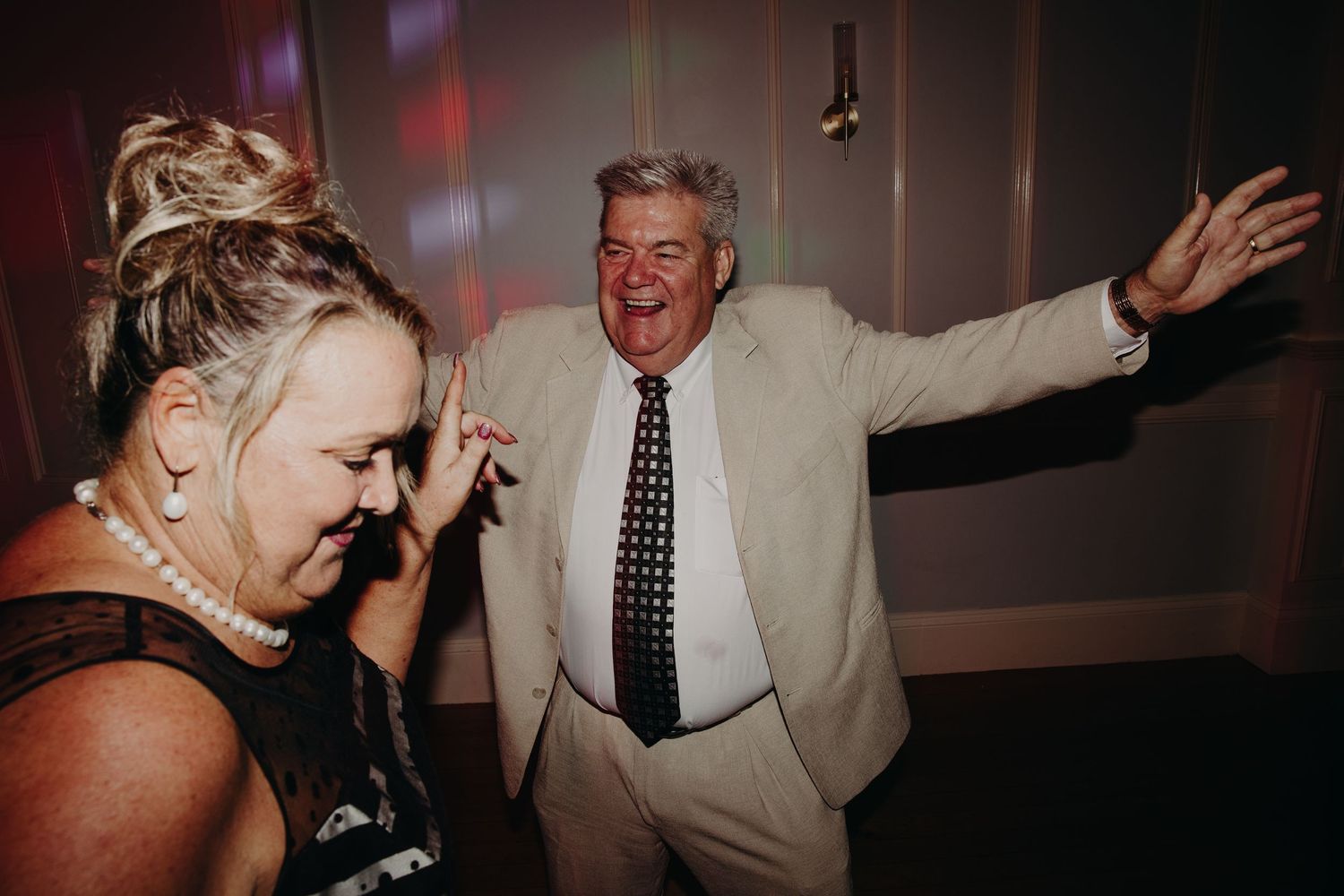 Wedding guests dancing and celebrating in a dimly lit reception venue.