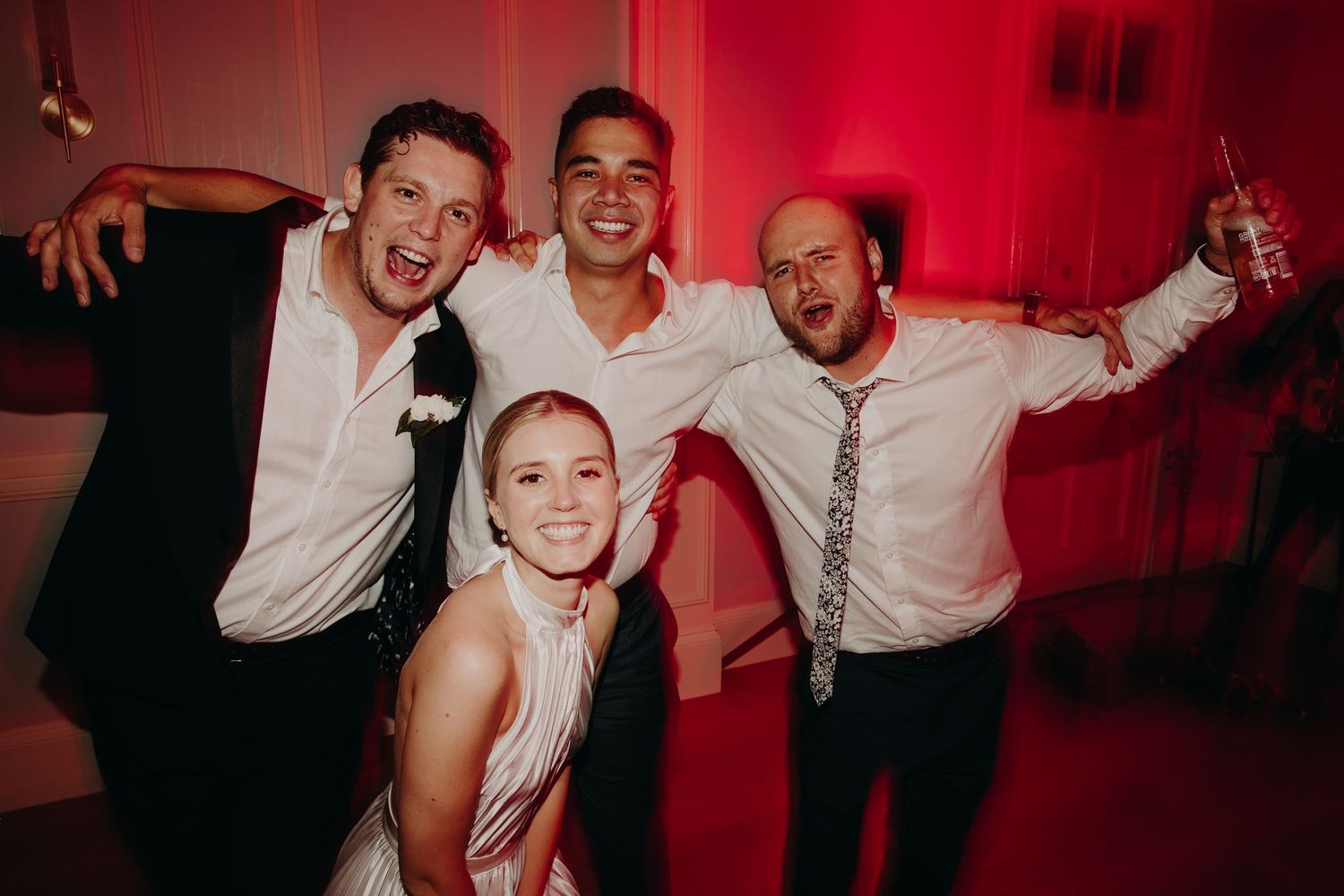 Wedding reception dance party with red mood lighting and energetic guests.