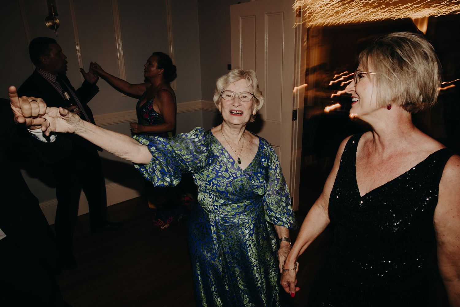 Wedding guests dancing and celebrating in an elegant venue with dramatic lighting.