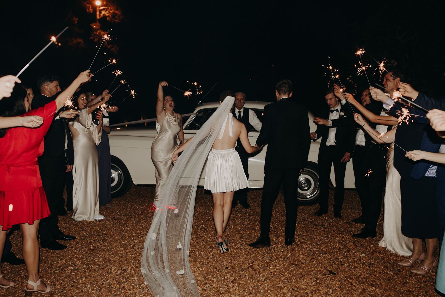 Wedding guests dance in a festive outdoor celebration at night with string lights overhead.
