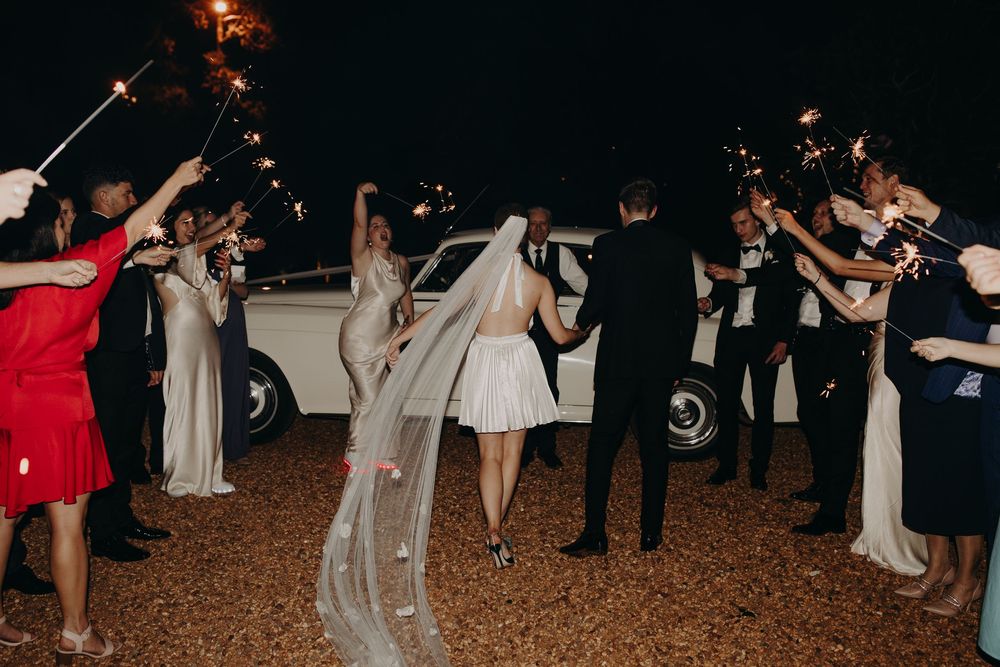 Wedding guests dance in a festive outdoor celebration at night with string lights overhead.