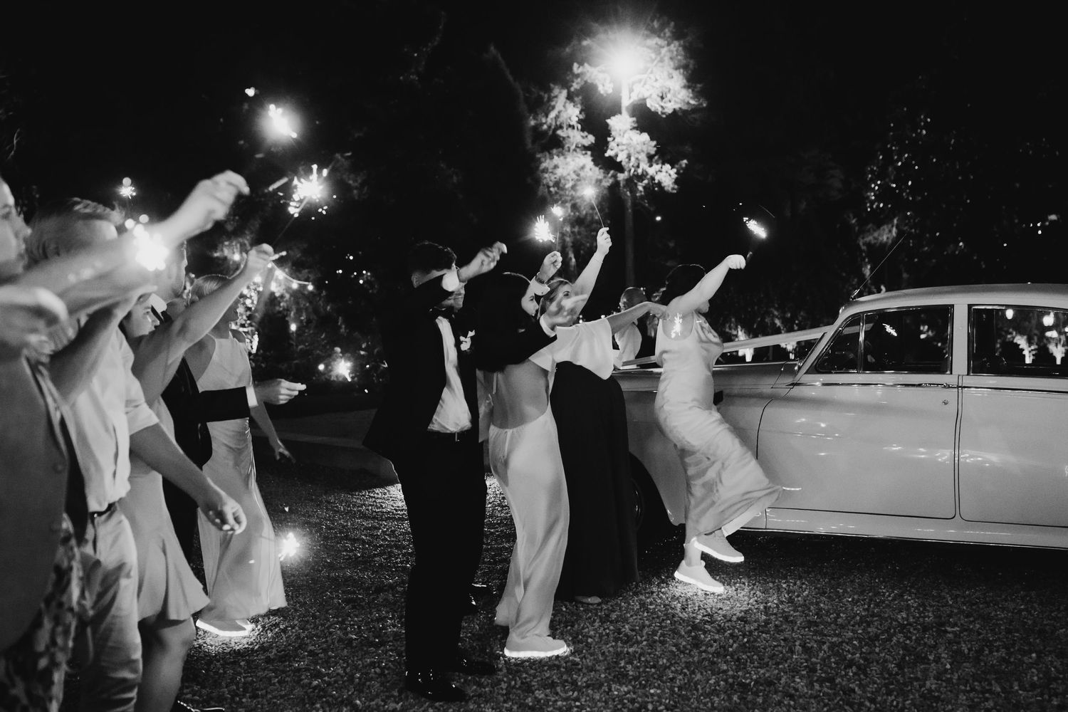 Wedding guests dance and celebrate on an outdoor dance floor at night with sparklers creating a magical atmosphere.