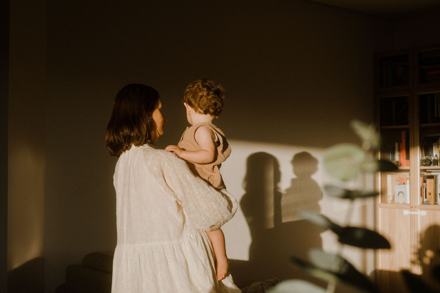 A silhouetted figure holds a child while their shadows cast on a sunlit wall.