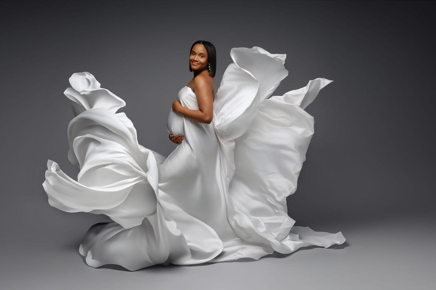 Artistic fashion portrait featuring flowing white fabric dramatically billowing around a figure against dark backdrop.