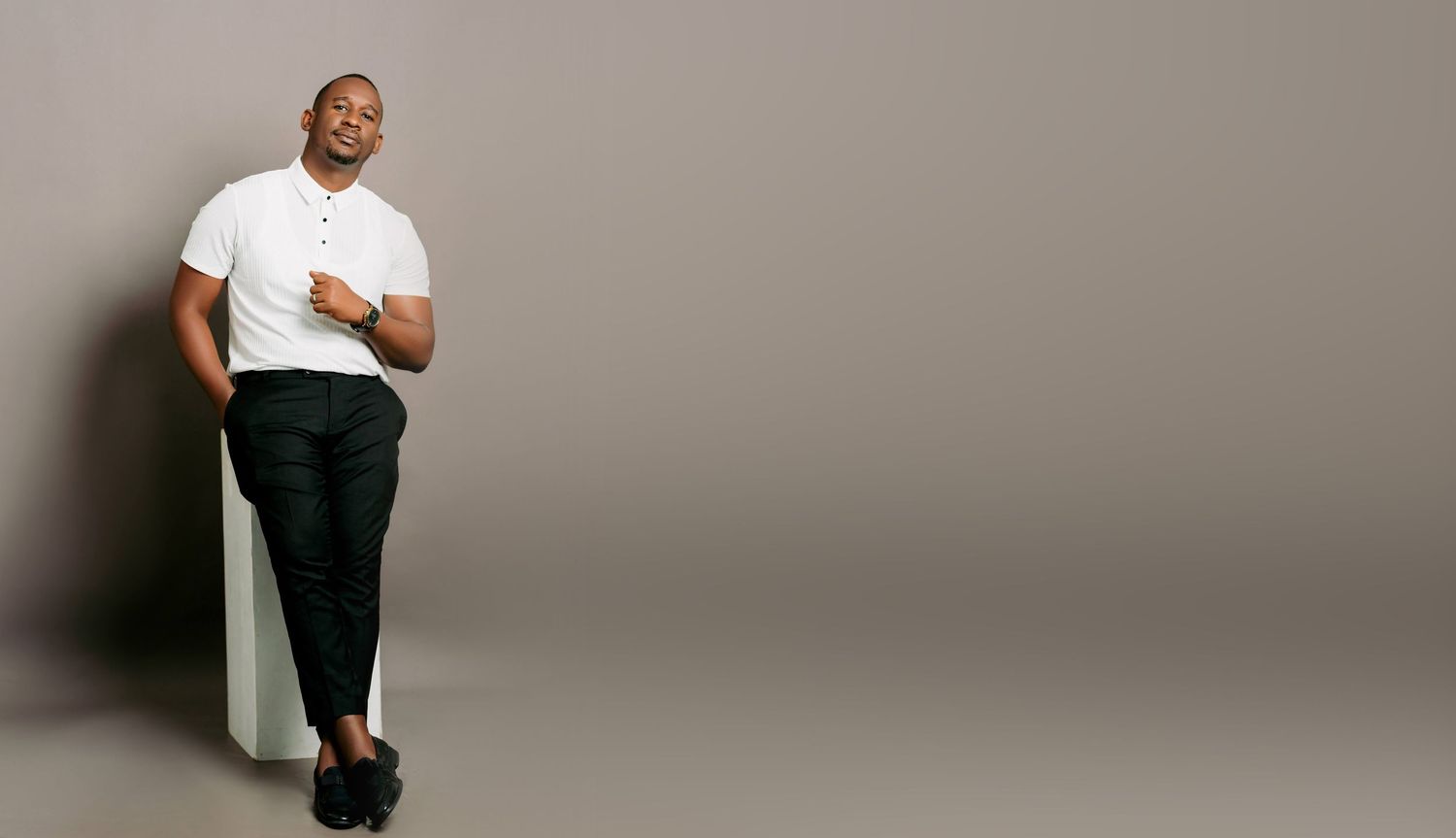 Casual portrait of person leaning against wall in white t-shirt and dark pants.