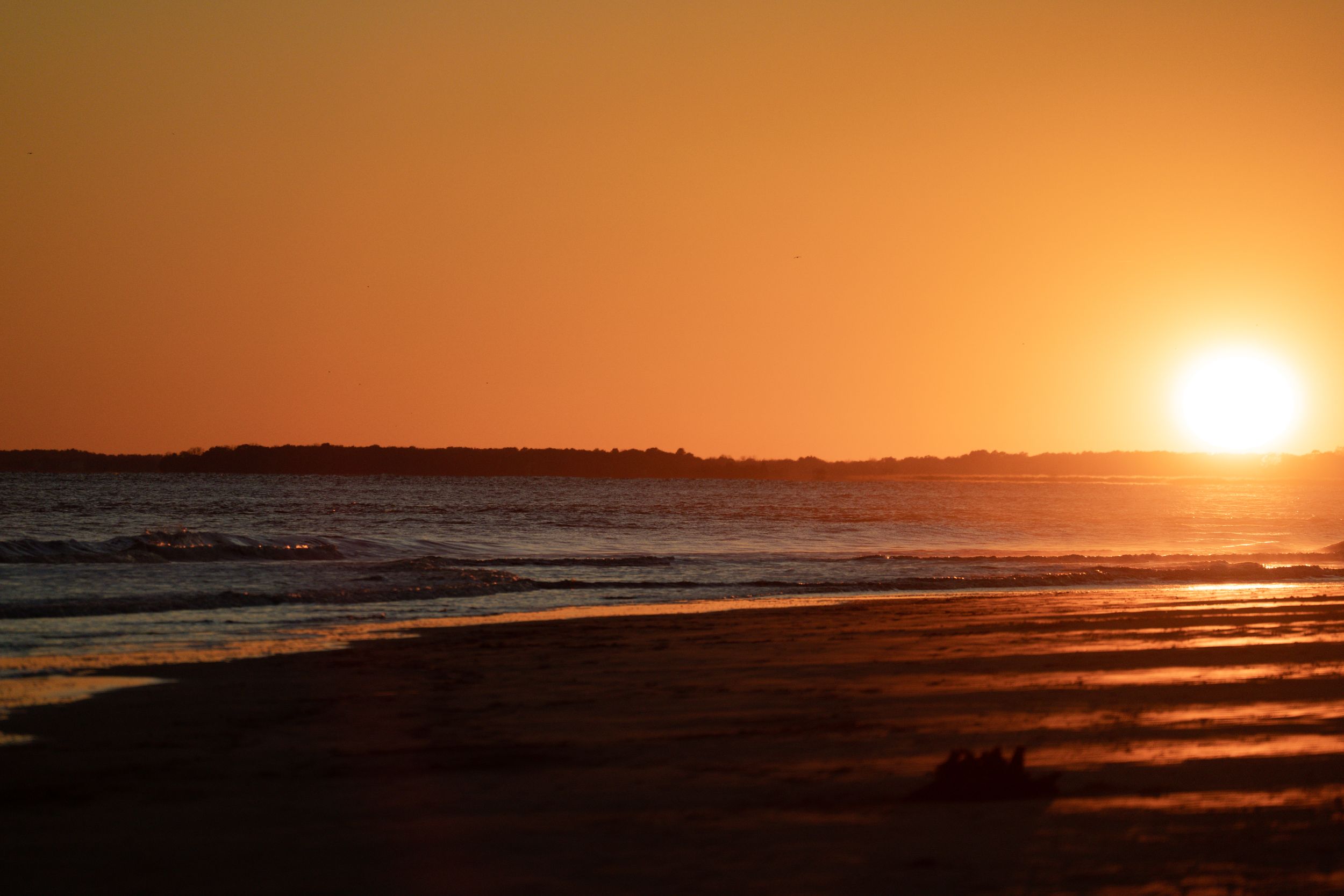 Golden sunset over the ocean horizon casting warm orange reflections on the beach.