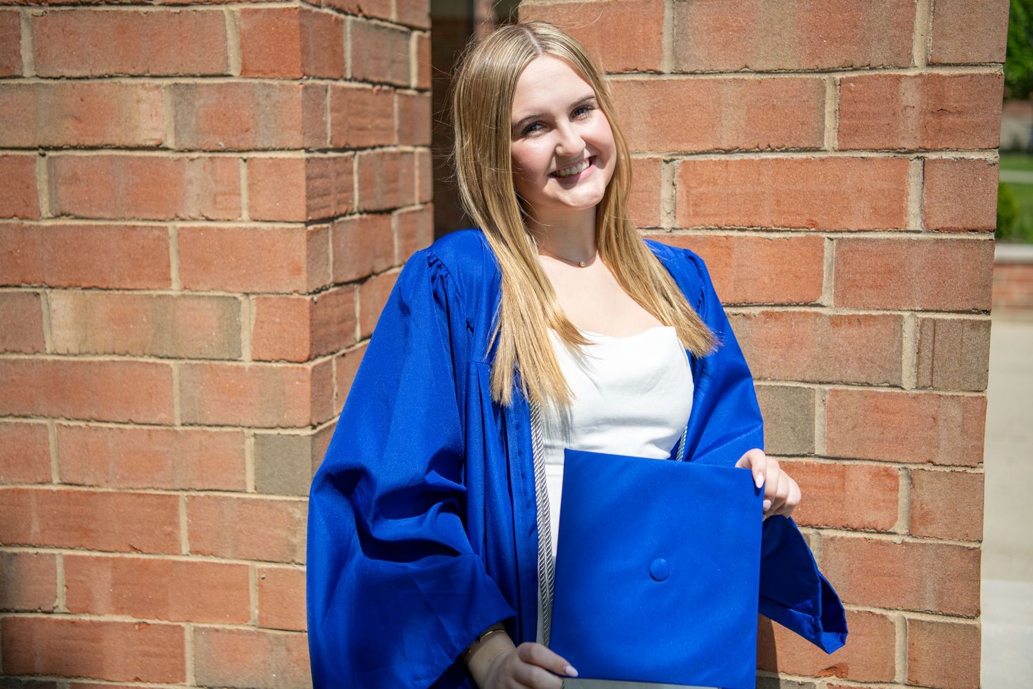 A person wearing a bright blue cardigan and white top stands against a brick wall.