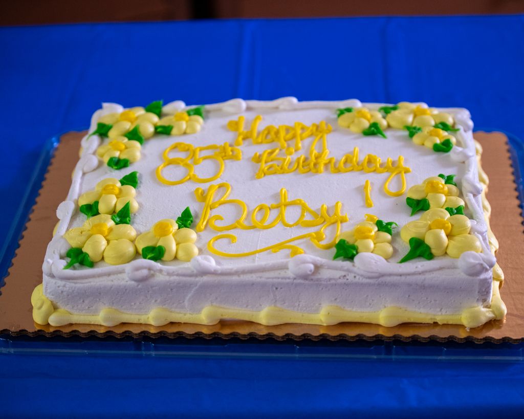 A long rectangular sheet cake with yellow frosting decorations and green accents on a blue background.