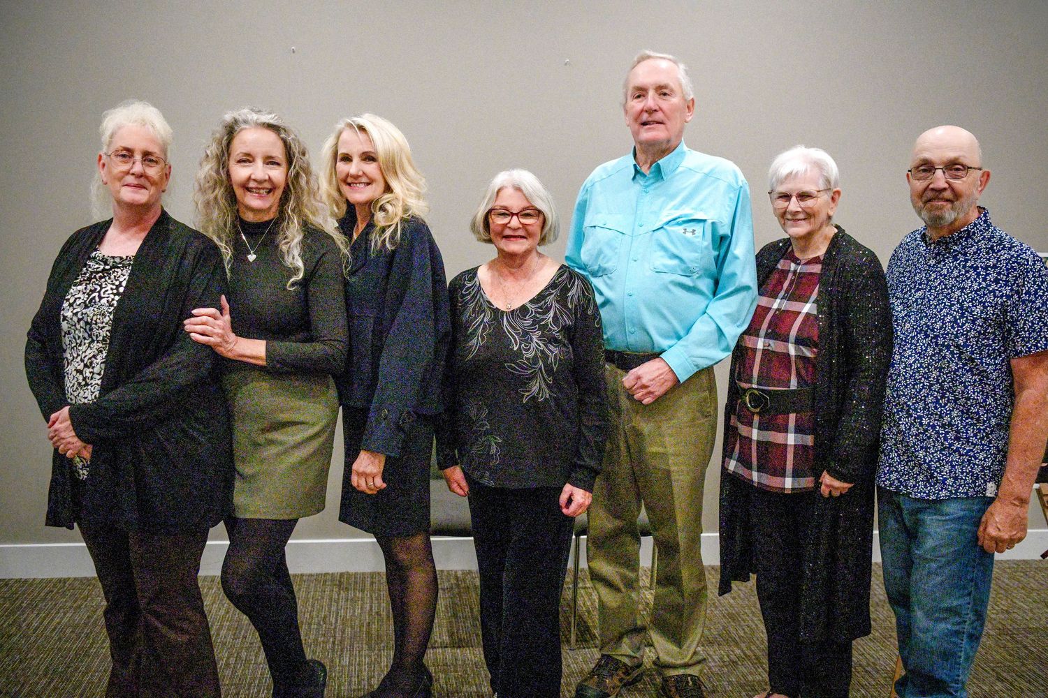 A group of seven people standing together and smiling for a casual indoor photo.