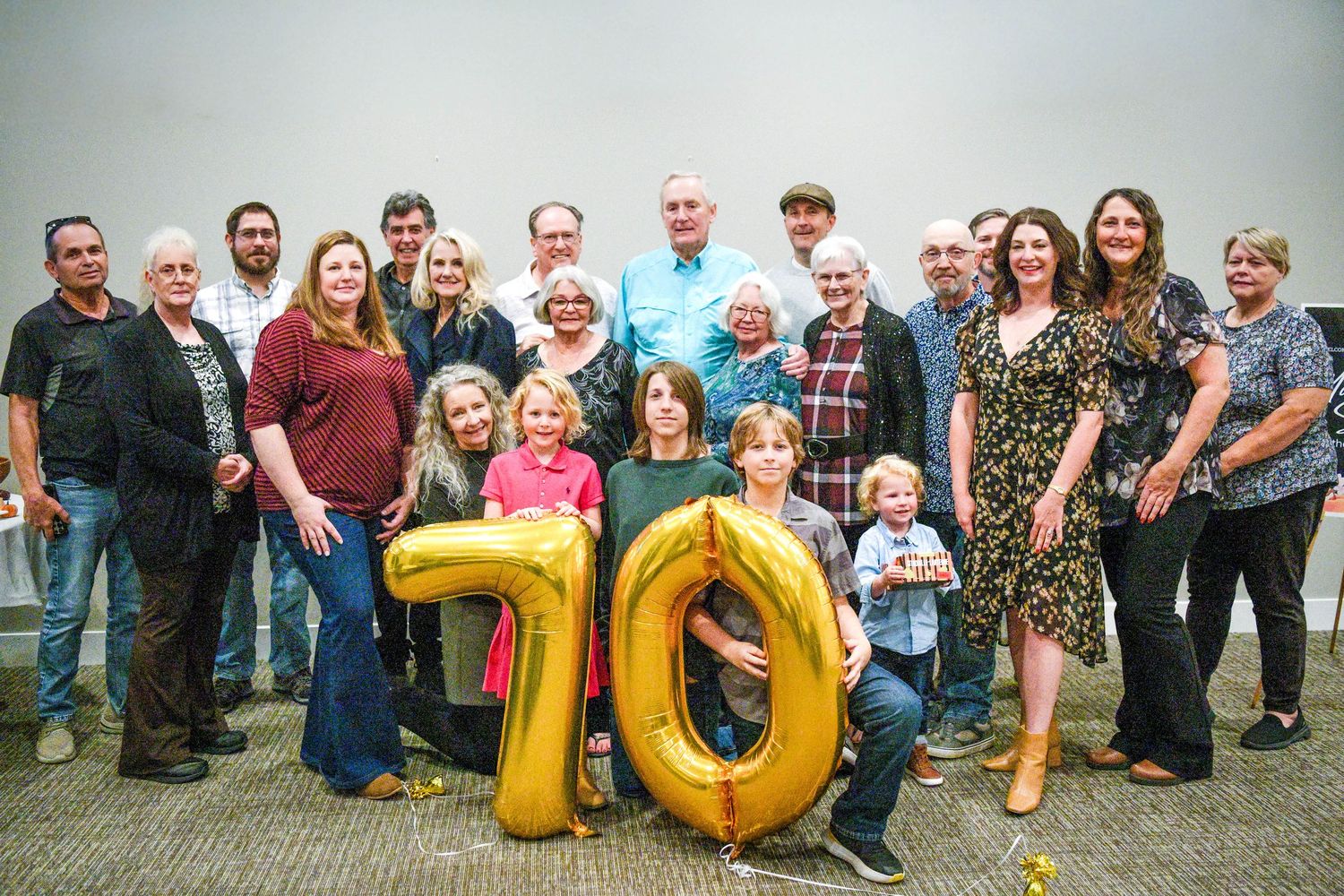 Large family group sitting outdoors on grass with gold number 70 balloons for anniversary celebration.