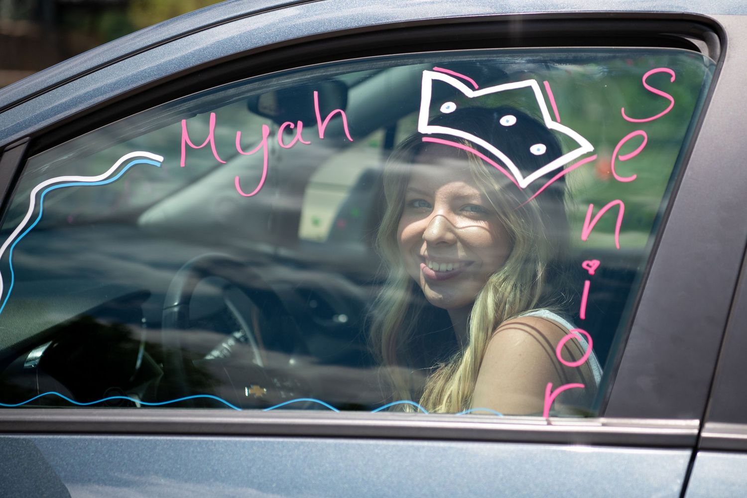 Car window decorated with pink cat ear drawings and text designs in neon colors.
