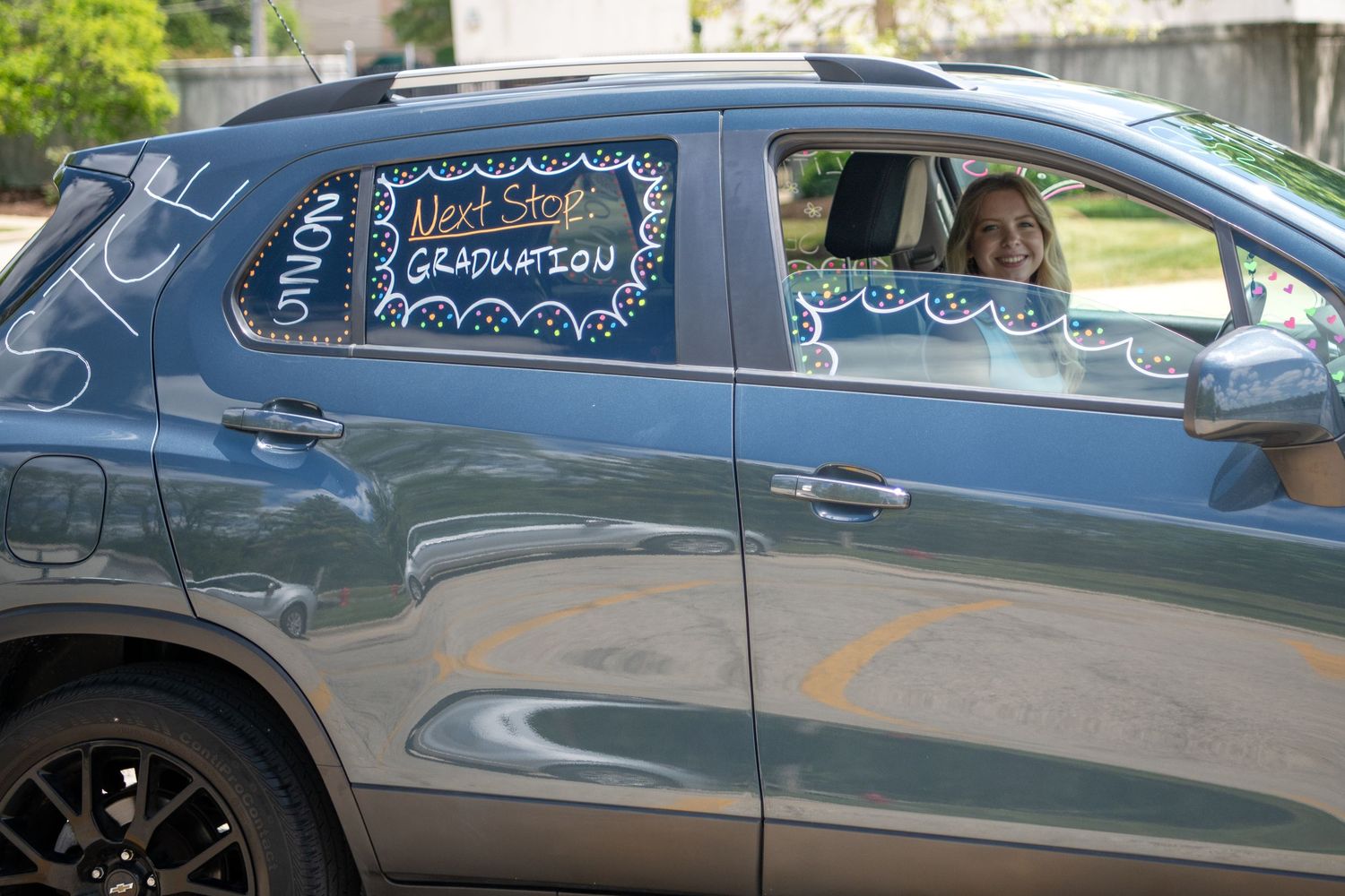Decorated car windows display graduation messages in white writing on a blue sedan.