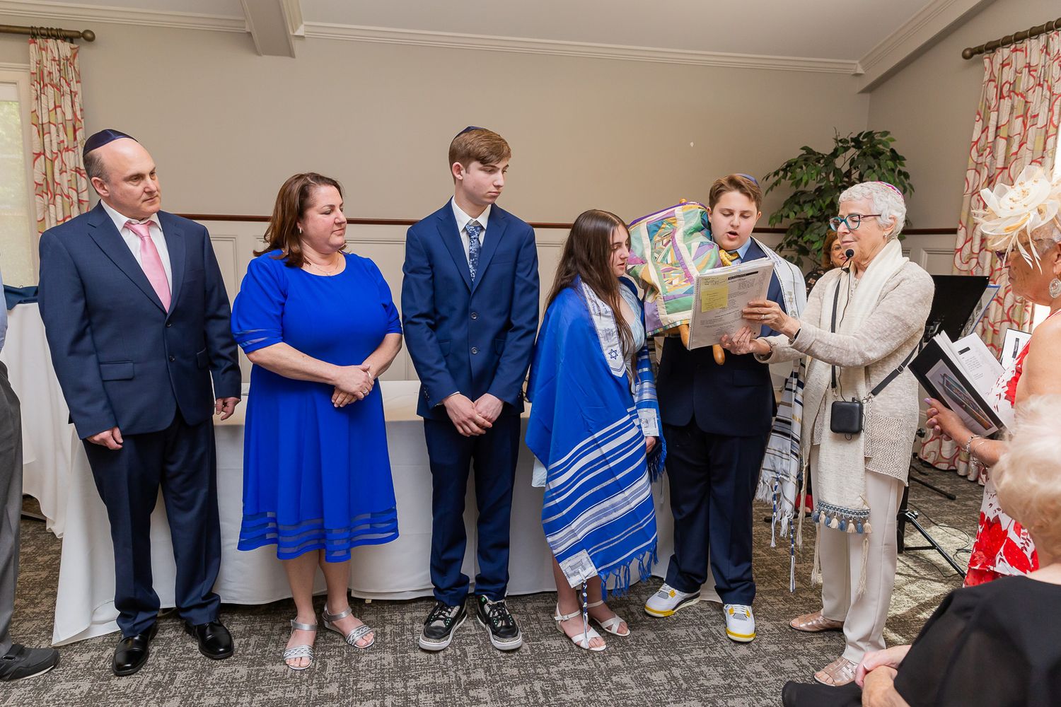 A group of people gather indoors for a ceremonial event wearing formal attire.