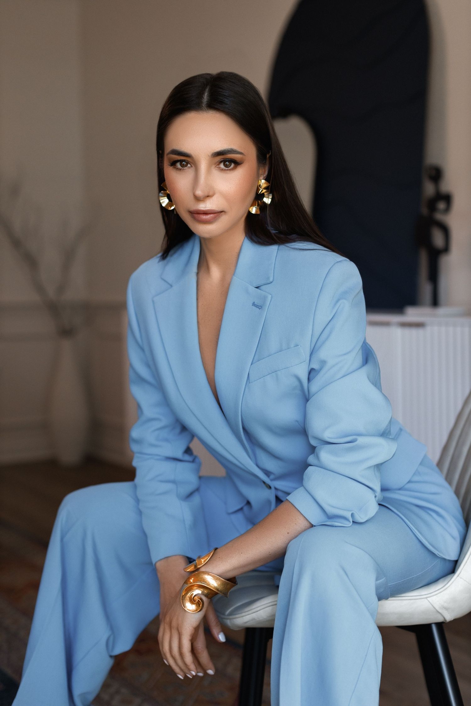 Portrait of a model wearing stylish light blue pantsuit sitting elegantly on chair.