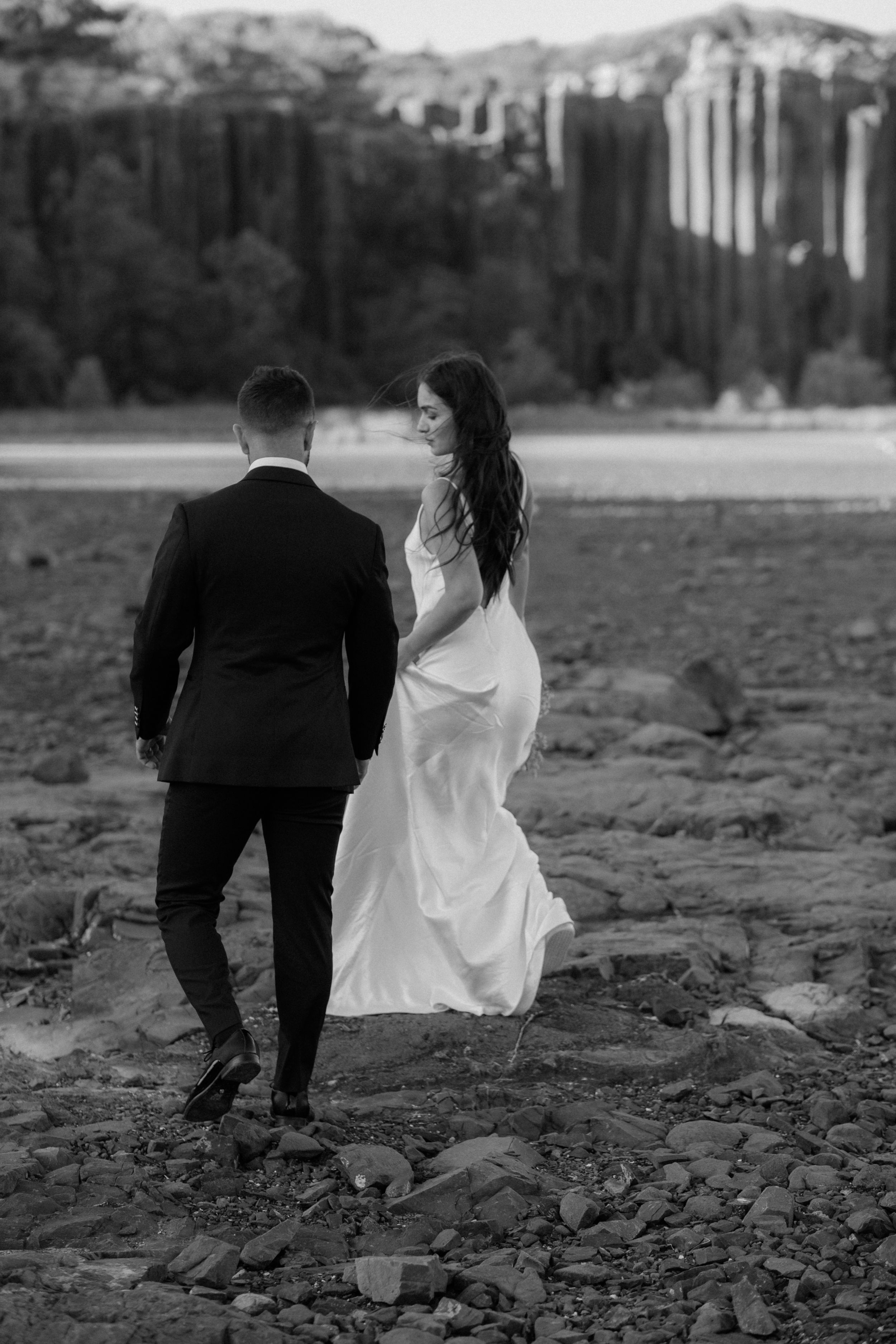 Bride and groom walking together on rocky terrain with mountains in the background.