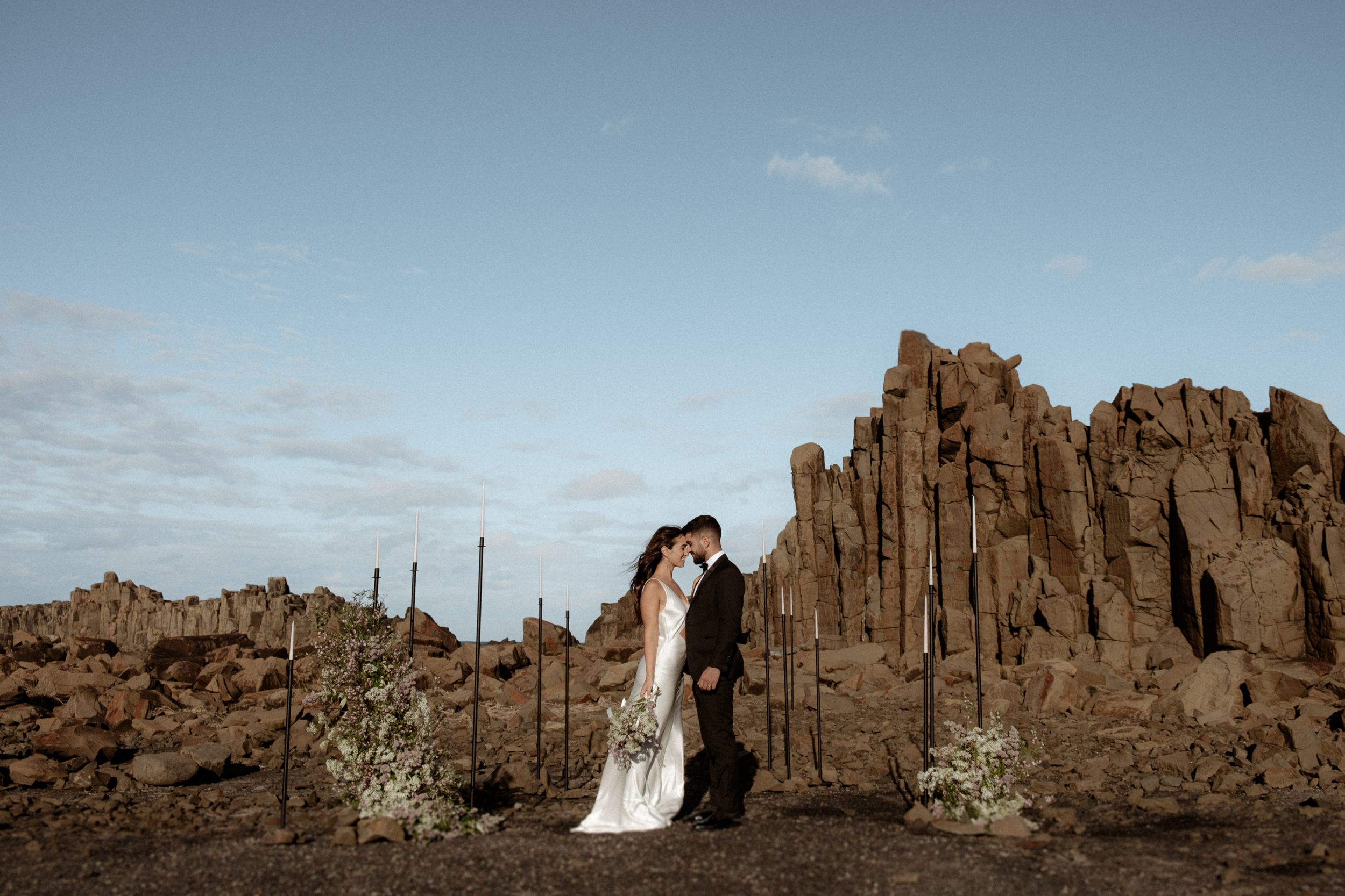 Wedding couple embracing in front of dramatic desert rock formations at sunset.