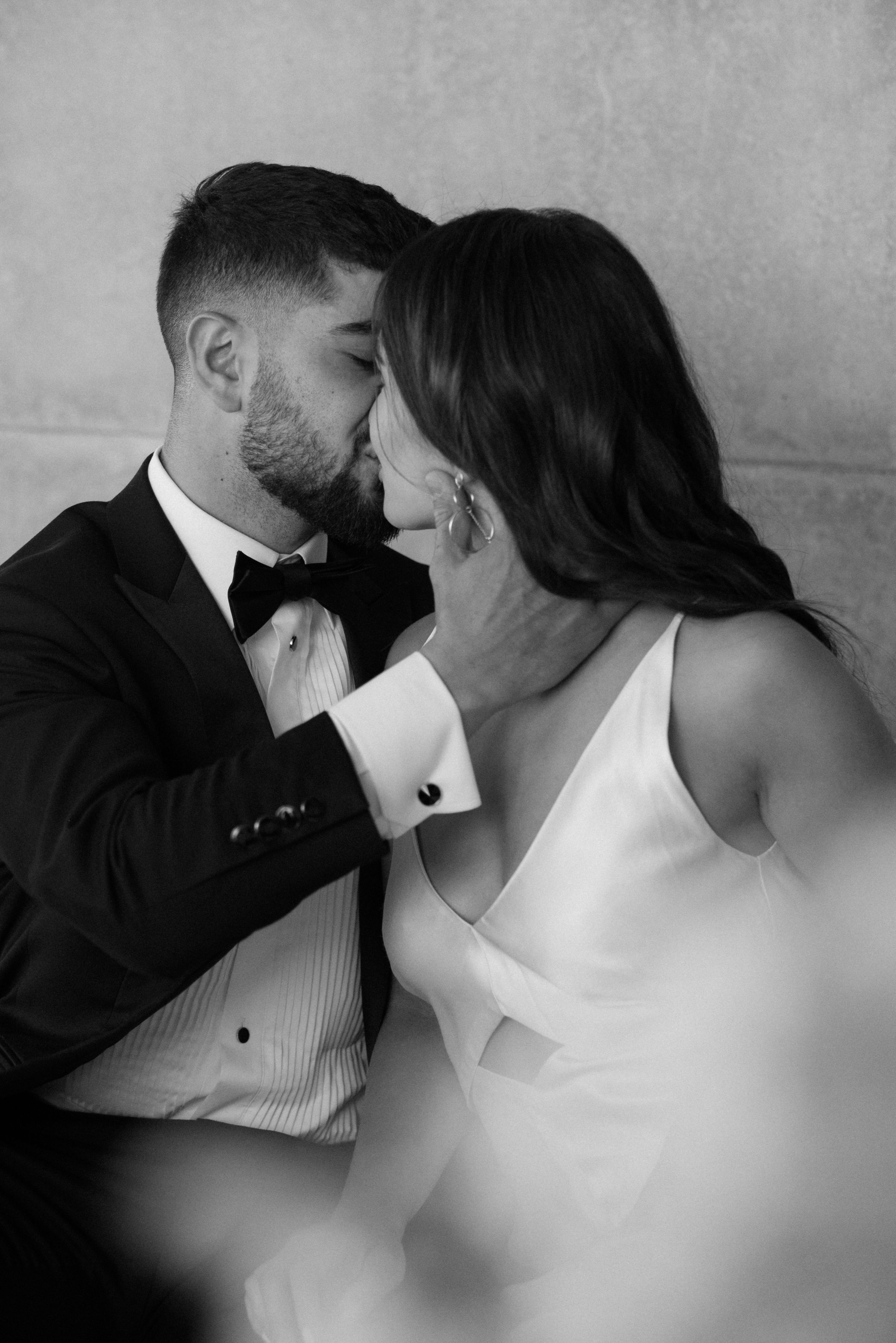 Intimate black and white portrait of a couple in formal wedding attire sharing a tender moment.